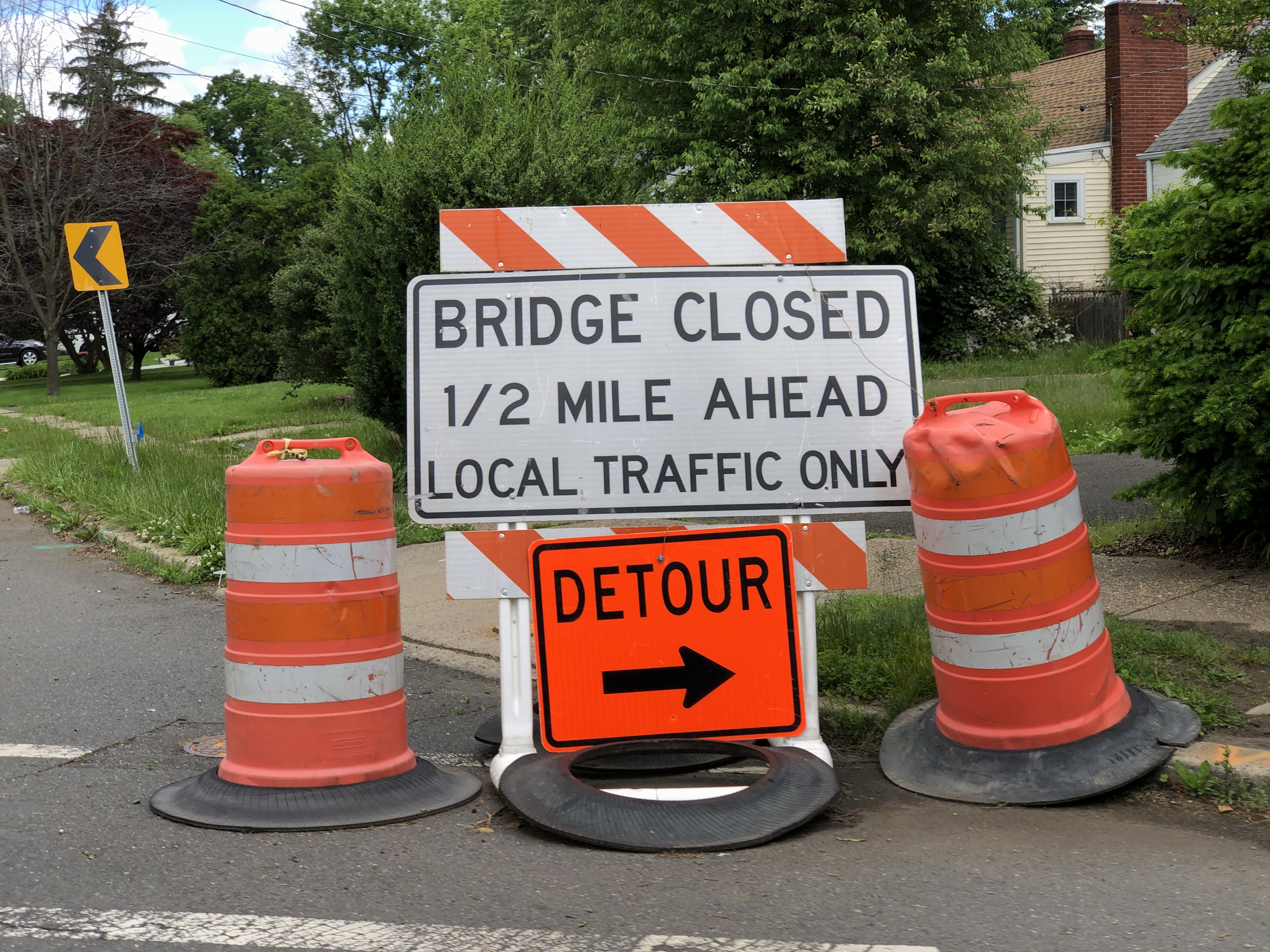 Orange traffic barrels flanking a bridge closed and detour sign on a road.