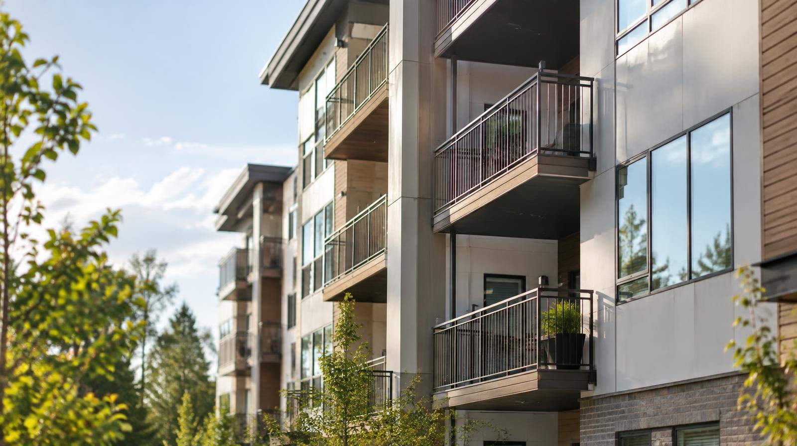 Modern multi-story apartment building exterior with balconies and large windows under a clear sky.