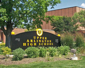 Monument sign for Upper Arlington High School with the school building visible behind trees.