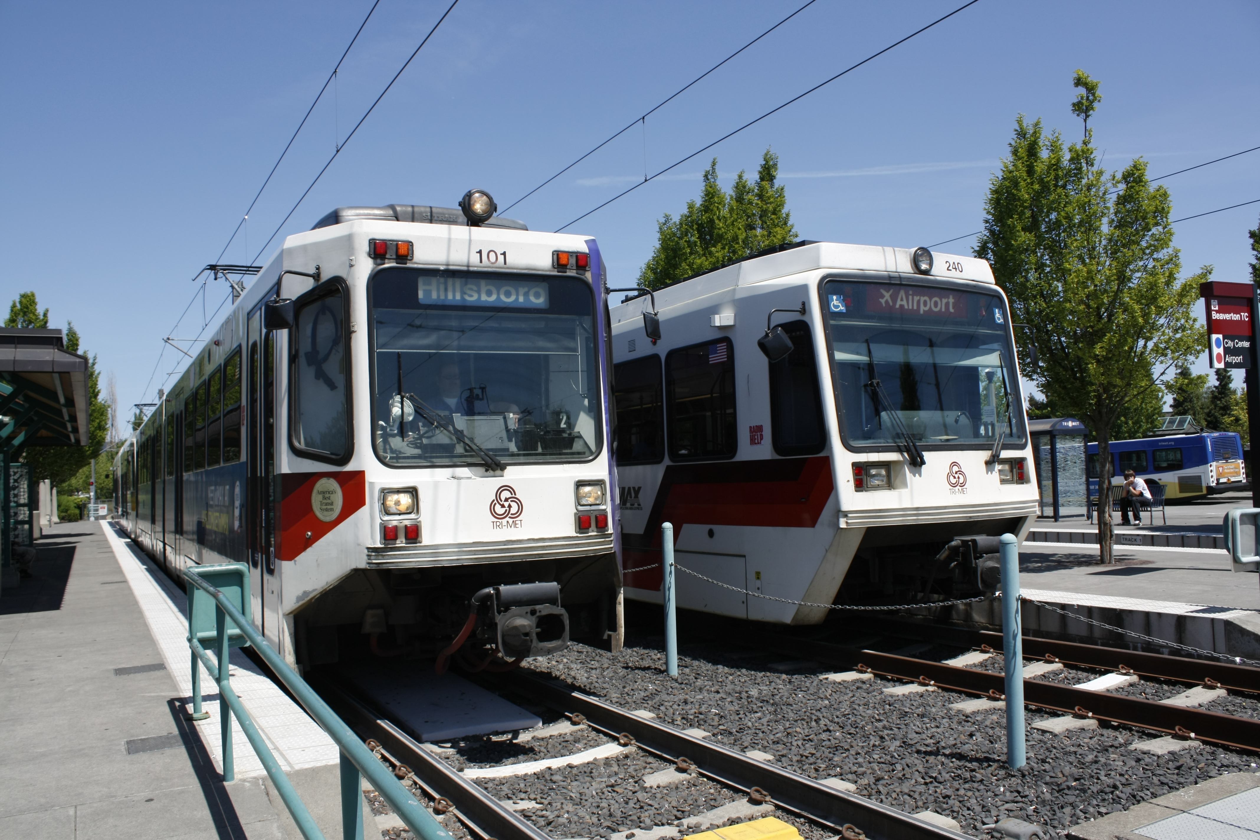 Two TriMet MAX light rail trains stopped side by side at a station platform.