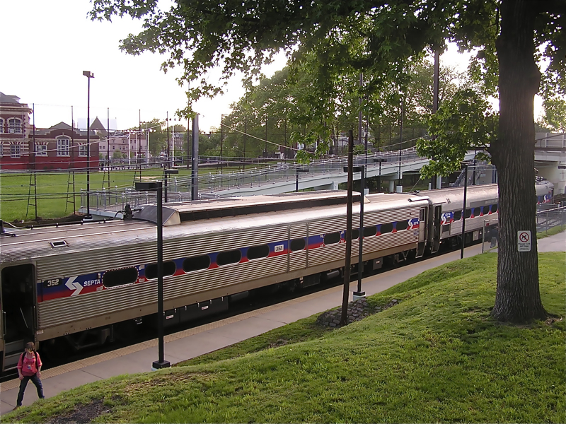 A SEPTA commuter train stopped at a station platform with trees and urban infrastructure nearby.