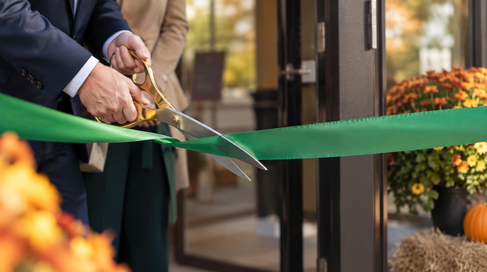 Large ceremonial scissors cutting a green ribbon across a doorway.