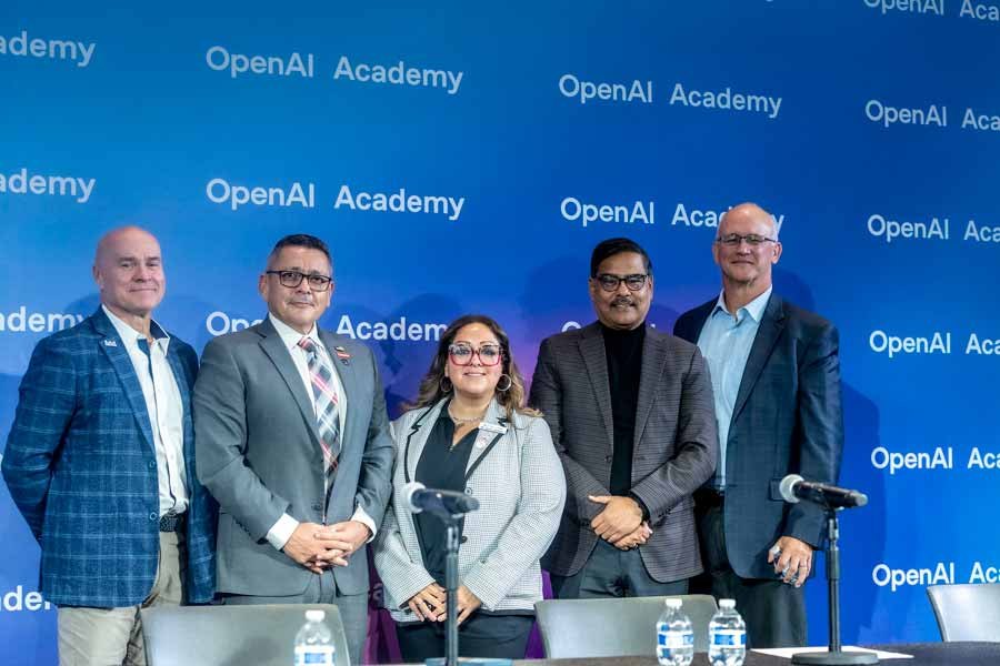 Five panelists stand behind a table on a stage with an OpenAI Academy branded backdrop.