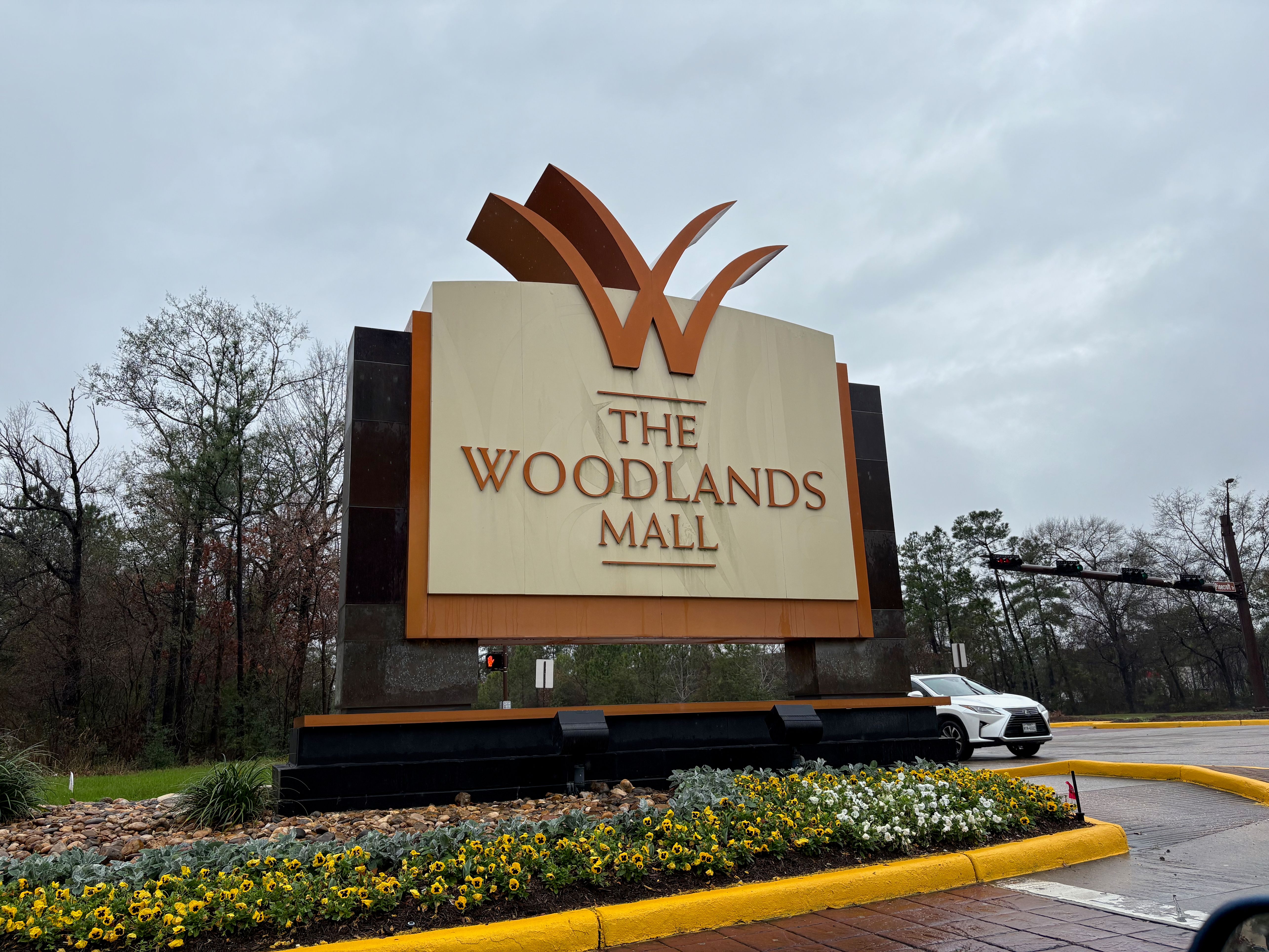 Entrance monument sign for The Woodlands Mall with a large stylized W logo and flowering plants.