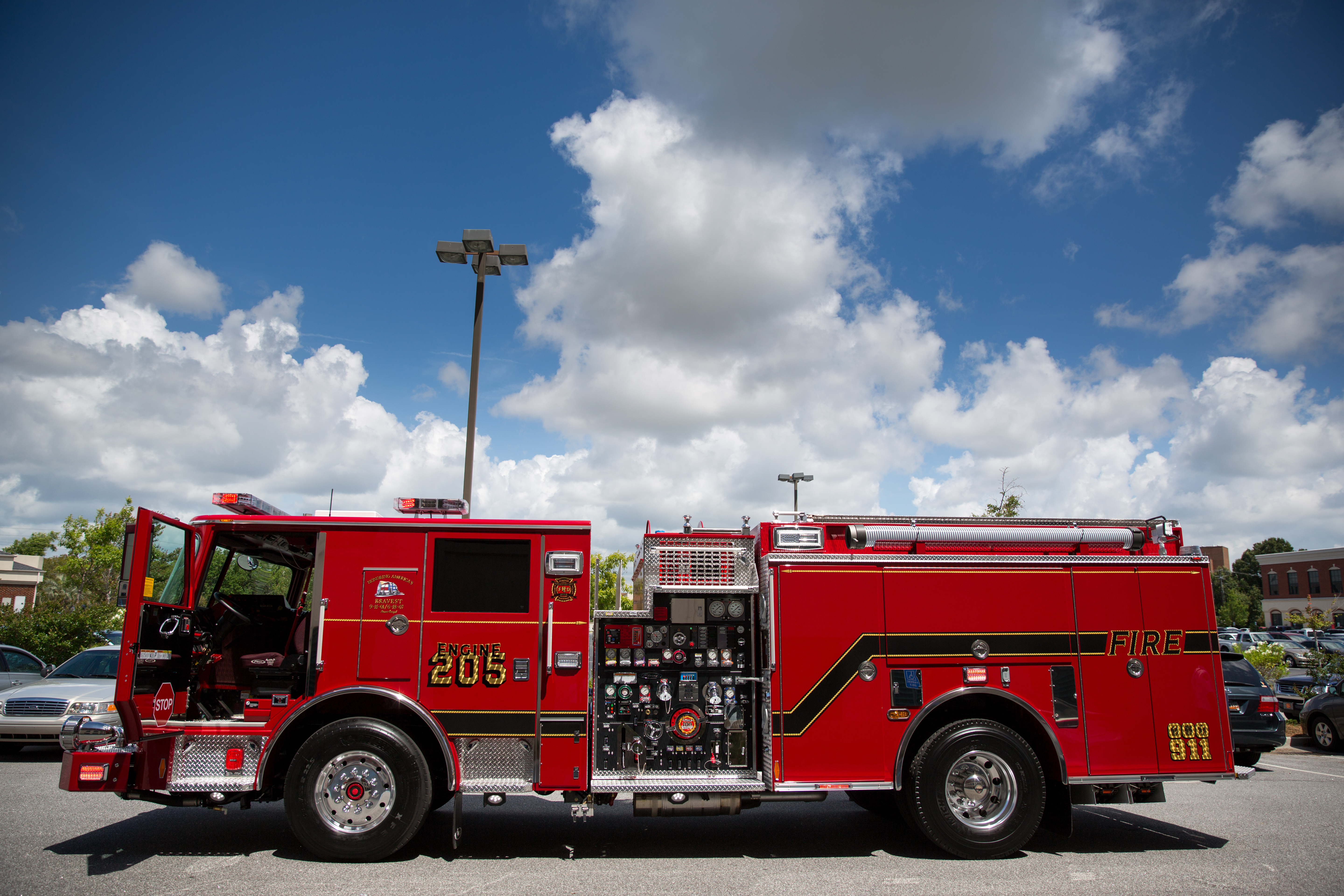 Red fire pumper truck with open side compartments parked in a parking lot.