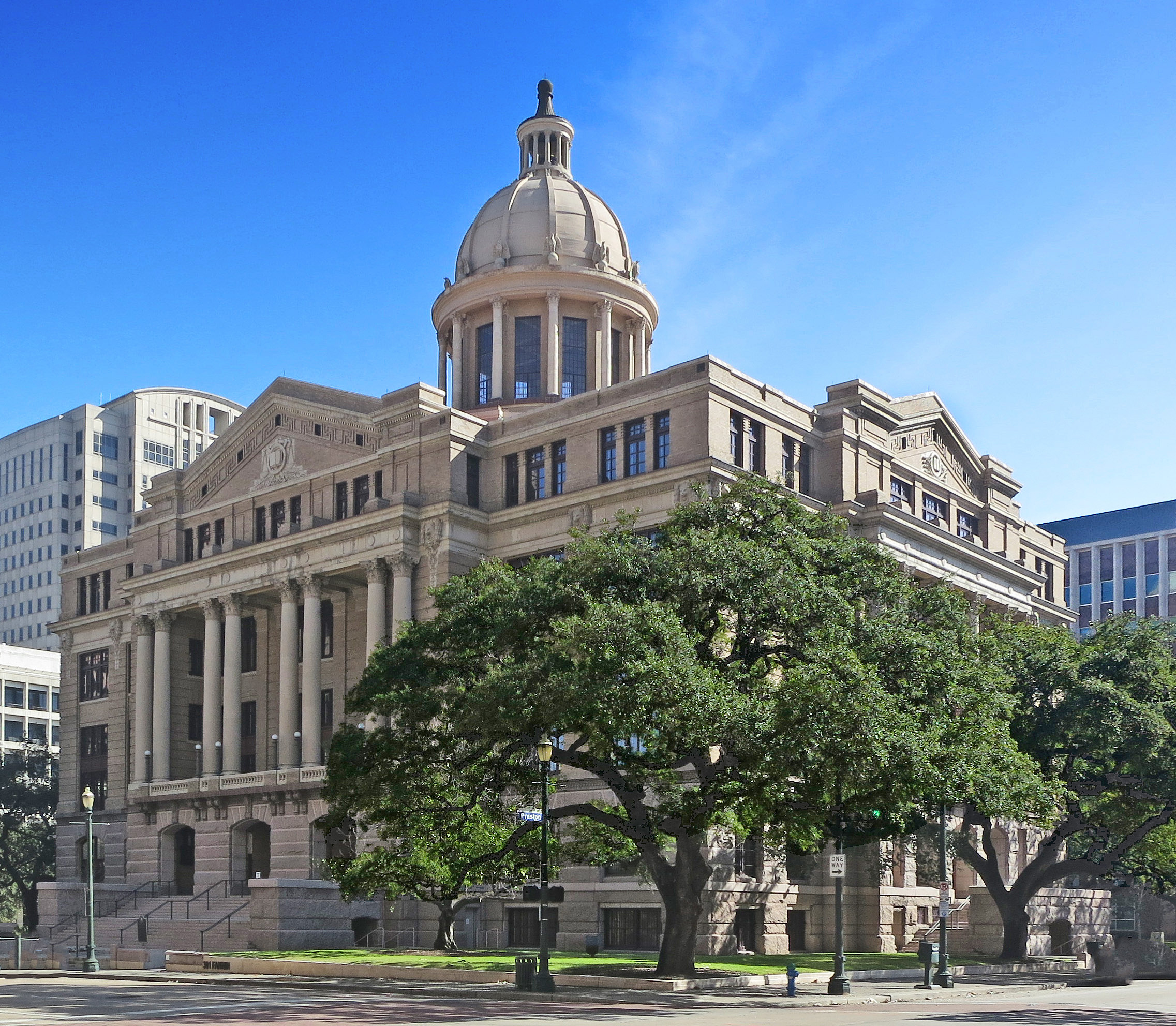 Neoclassical domed courthouse with Corinthian columns and oak trees in front.