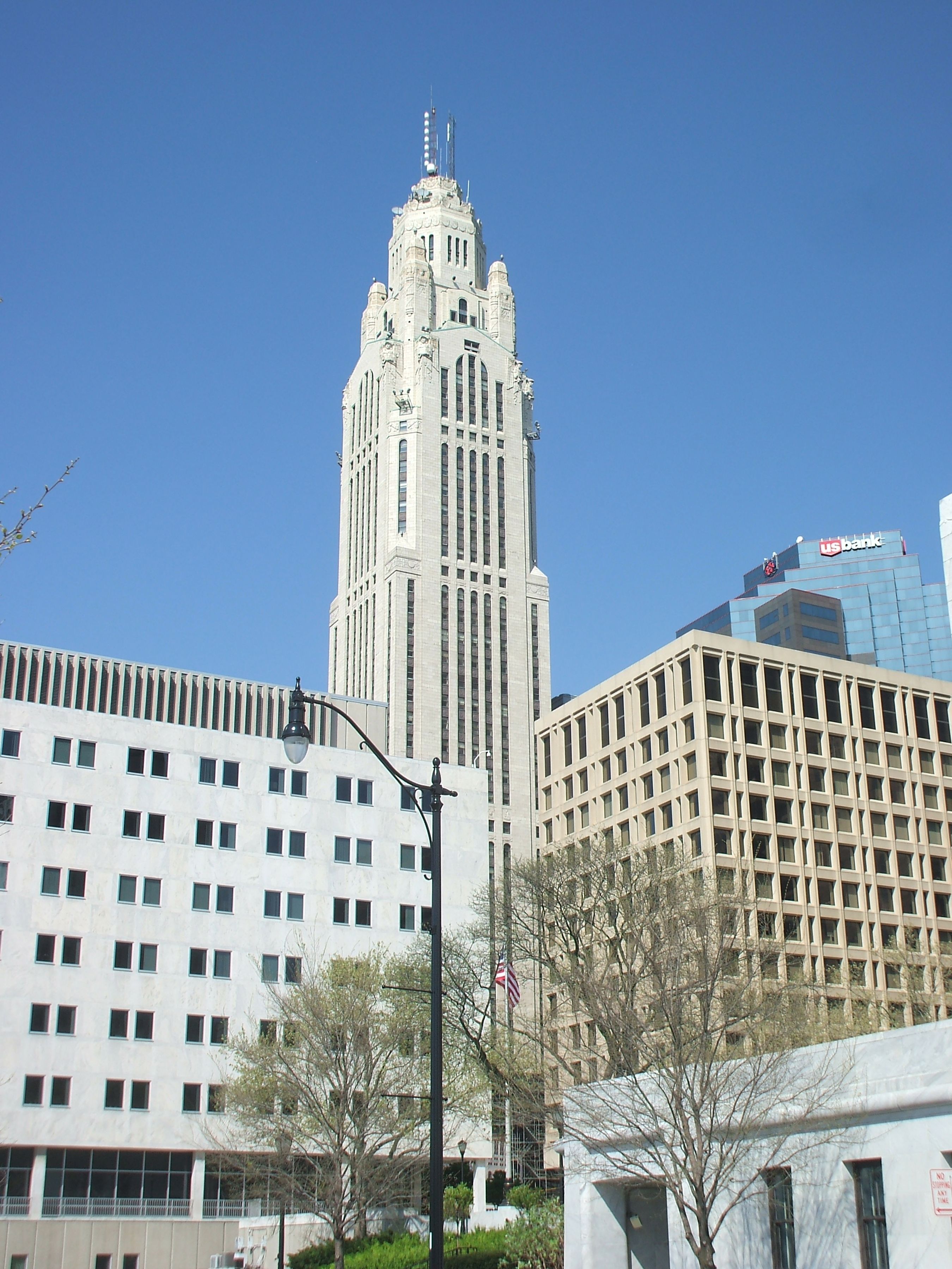 Tall Art Deco office tower surrounded by lower commercial buildings under a blue sky.