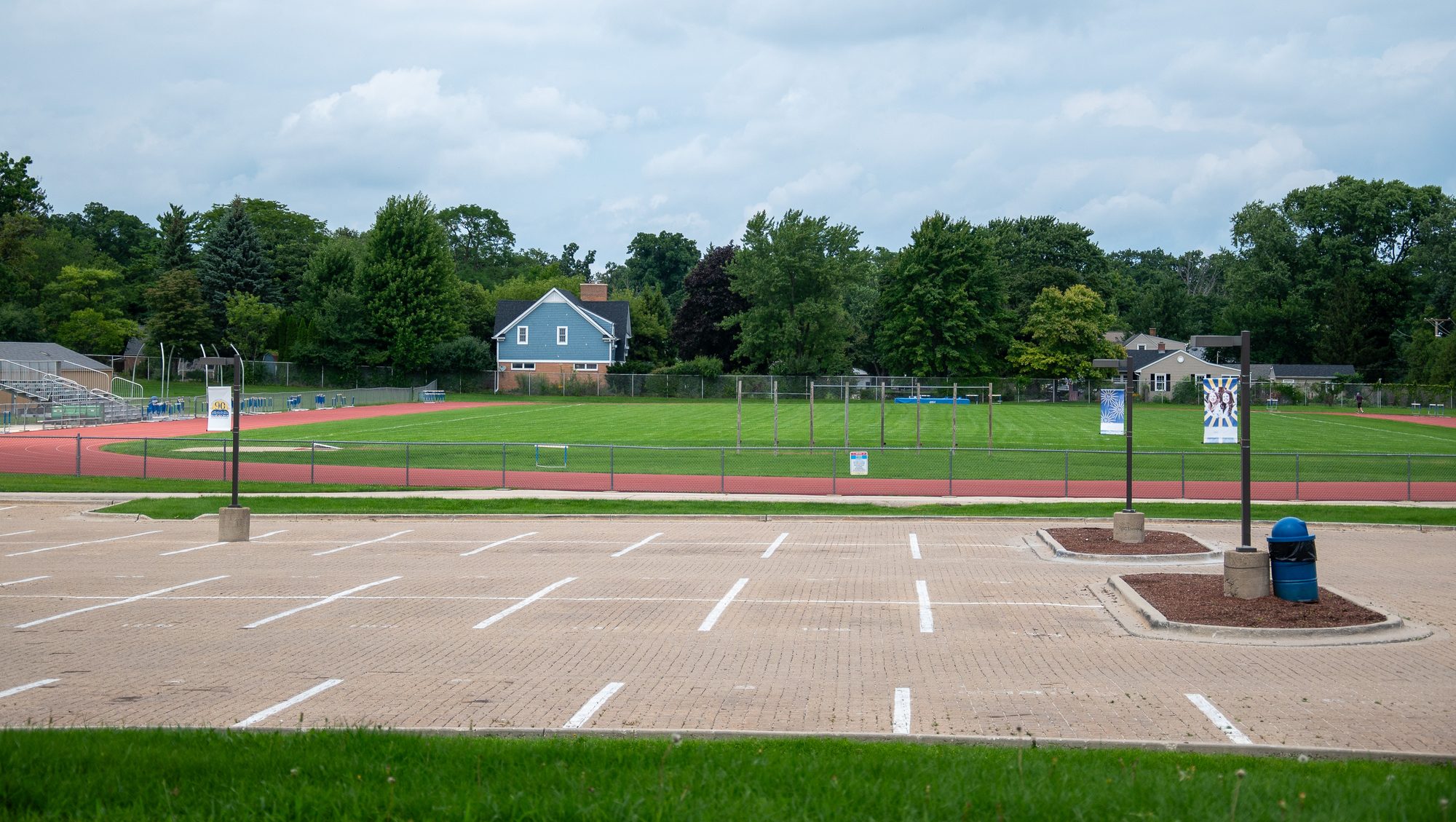 Empty parking lot beside a running track and green athletic field with bleachers