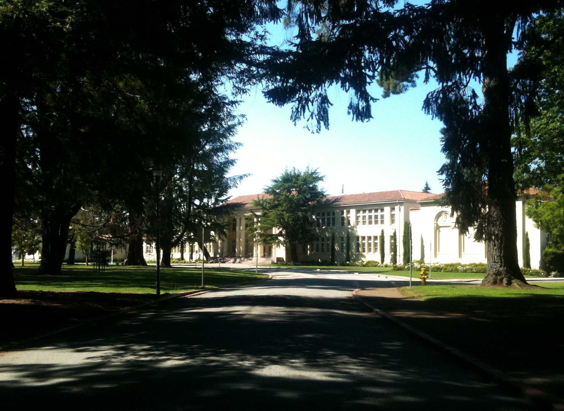 Two-story classical school building with arched windows, lined by tall trees.