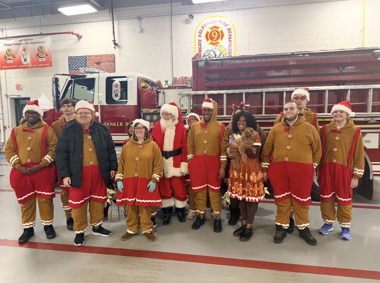 Group of people in gingerbread costumes and Santa hats posing in front of a fire truck.