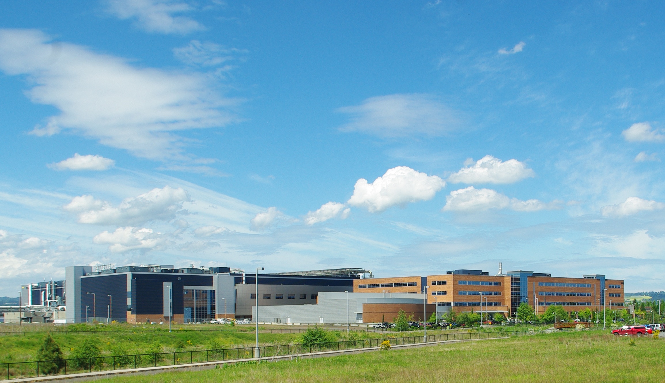 Large multi-building industrial campus with brick and metal-clad structures under a partly cloudy sky.
