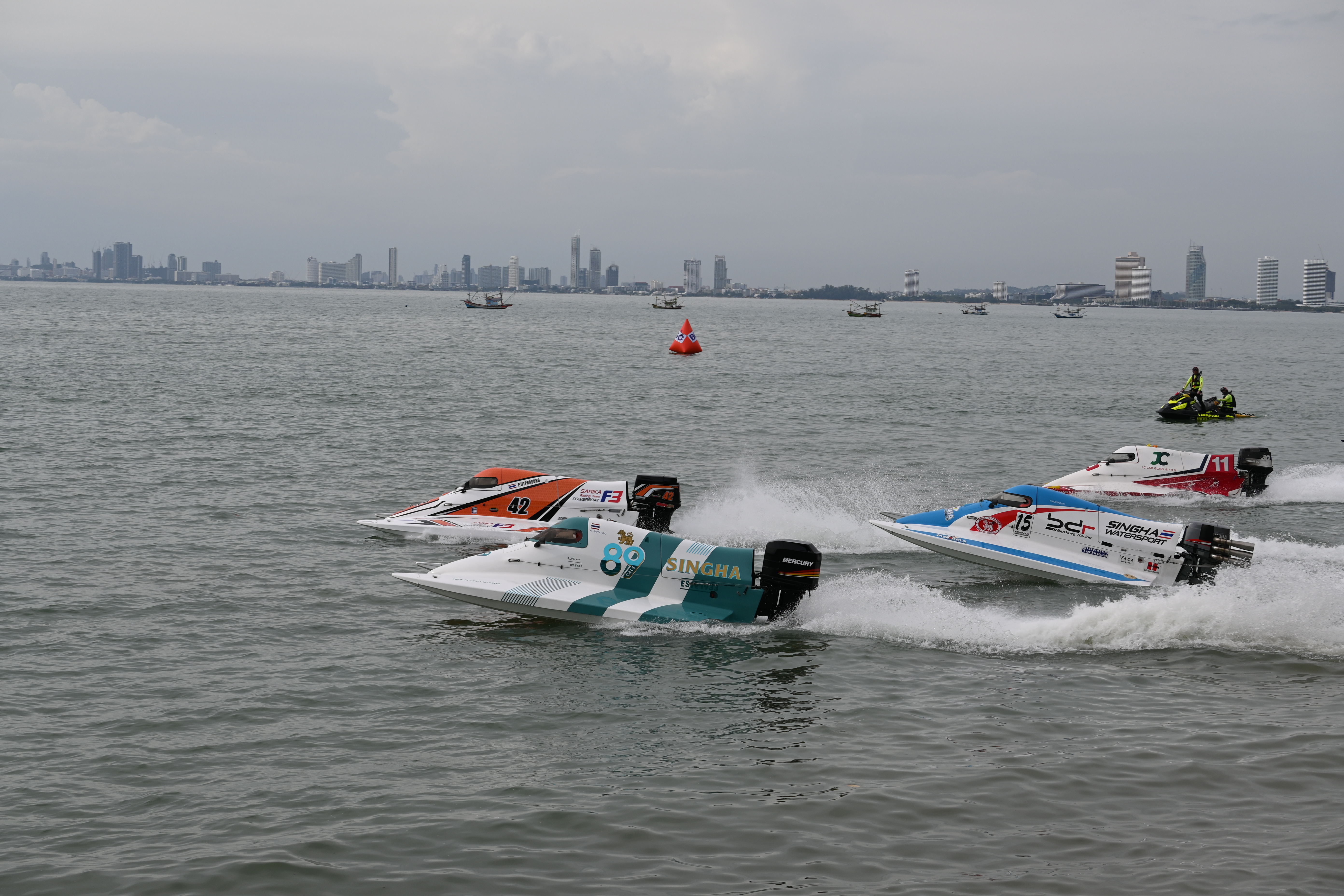 Three colorful racing powerboats speeding across choppy water near a city skyline.