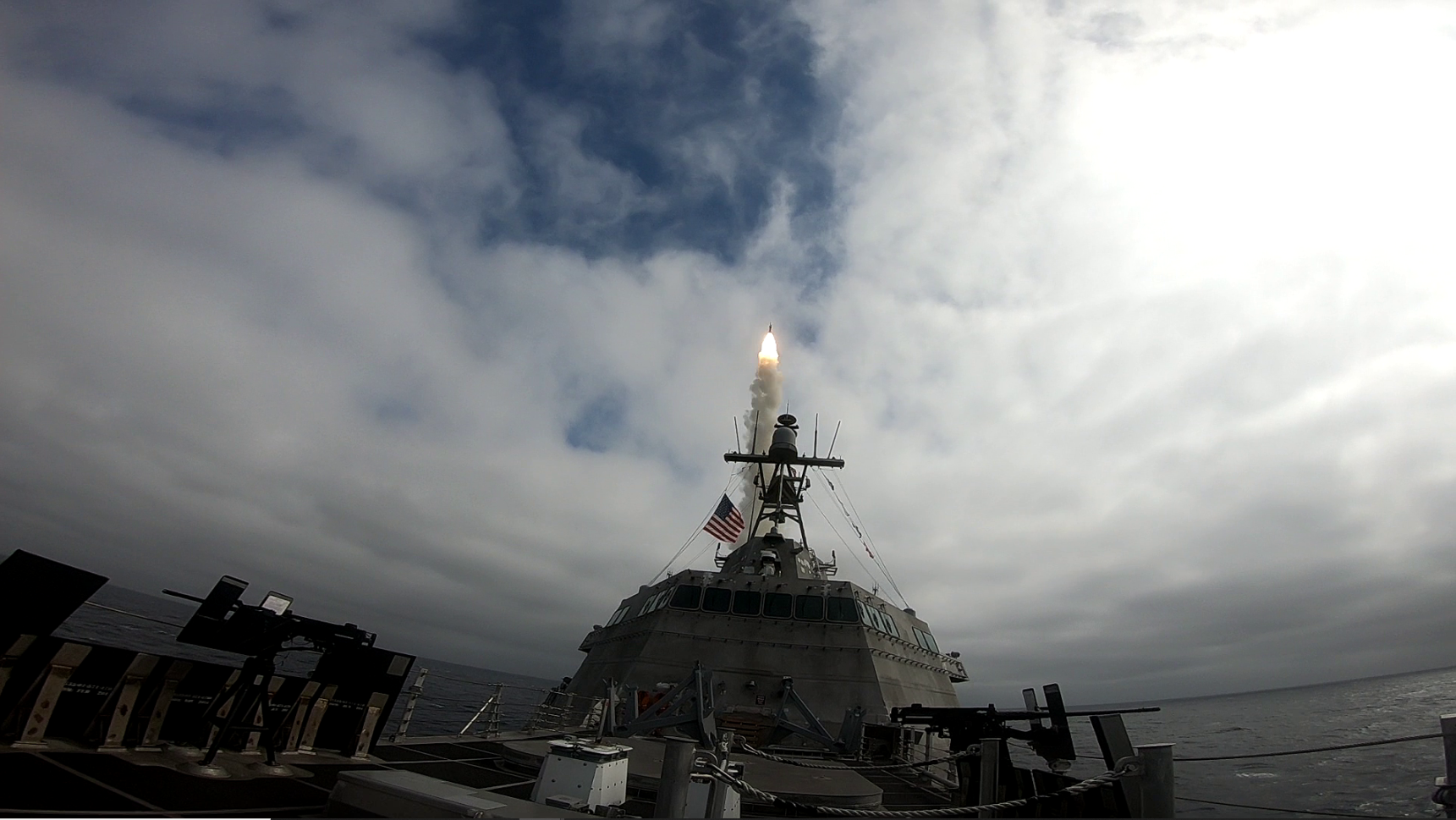 Navy ship at sea launching a missile with a bright flame and smoke trail.