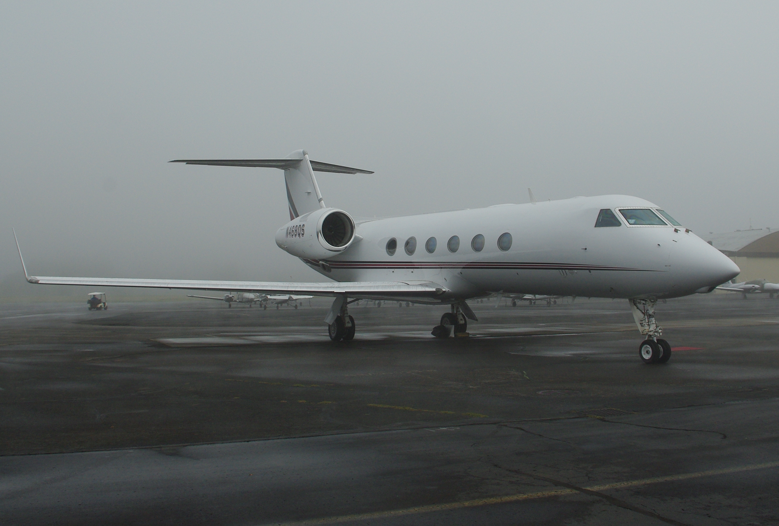 White business jet parked on a wet tarmac at a regional airport under overcast skies.