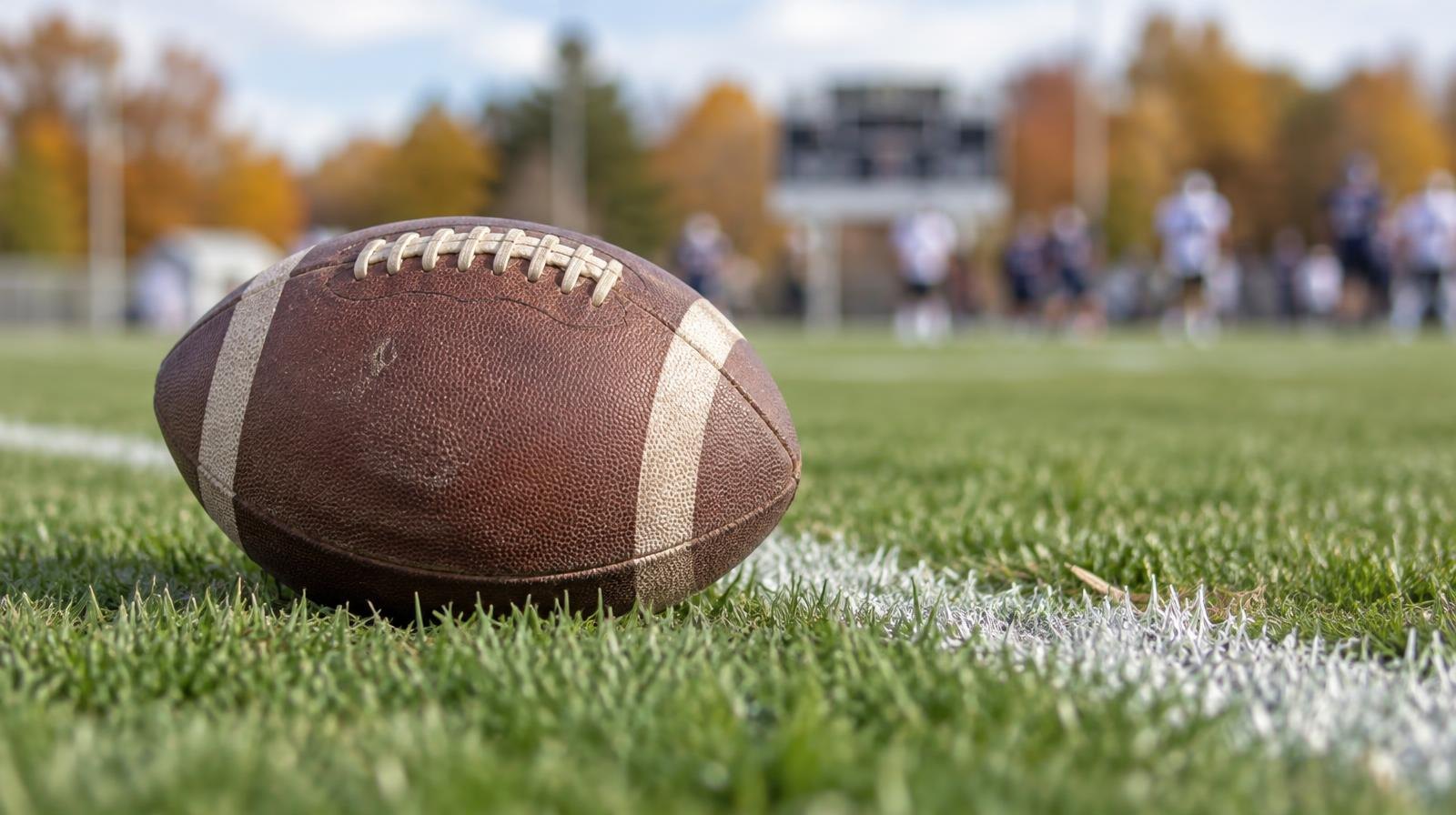 An American football resting on green grass beside a painted white yard line.