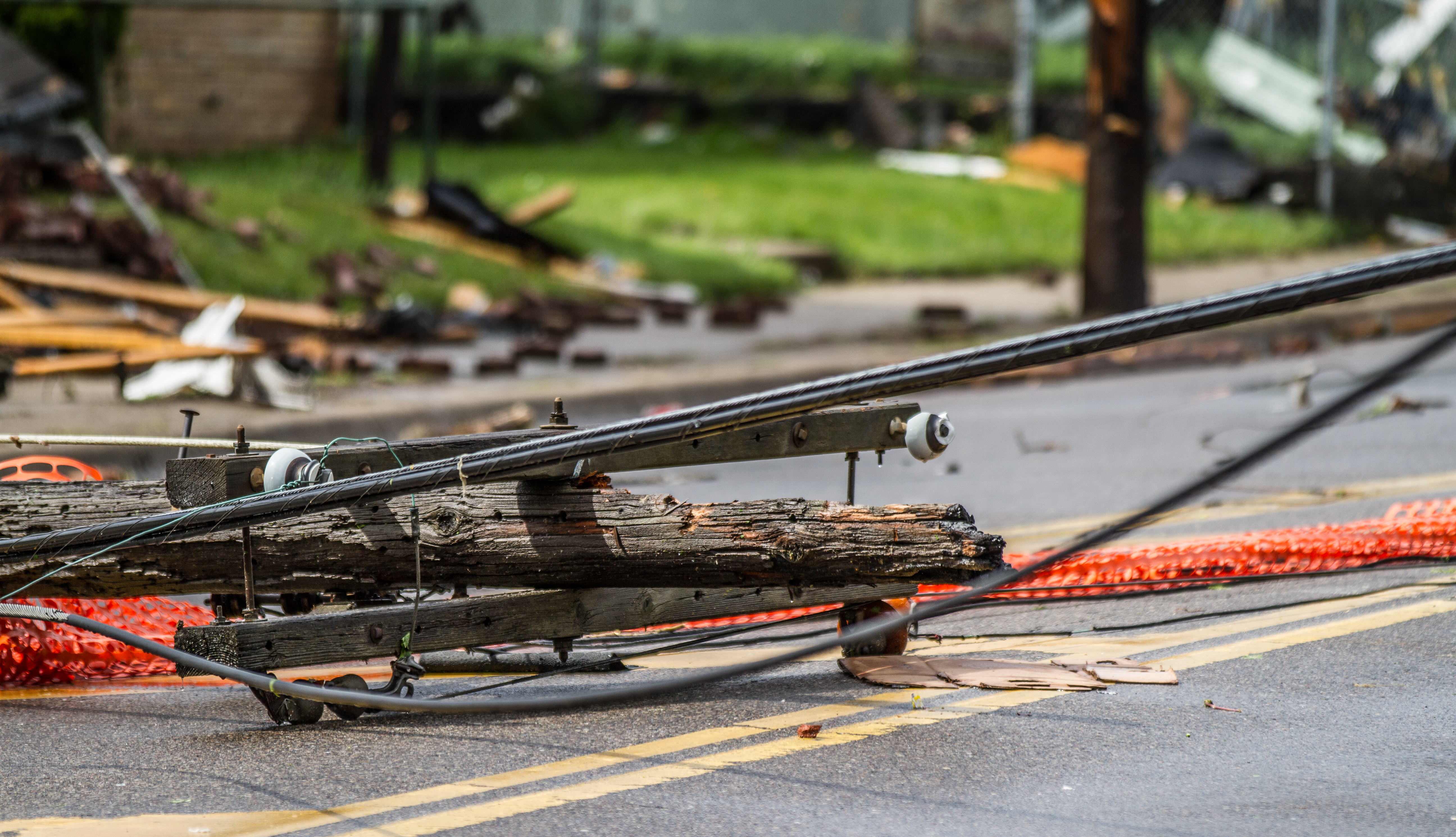 Snapped utility pole and downed power lines lying across a road with safety barriers.