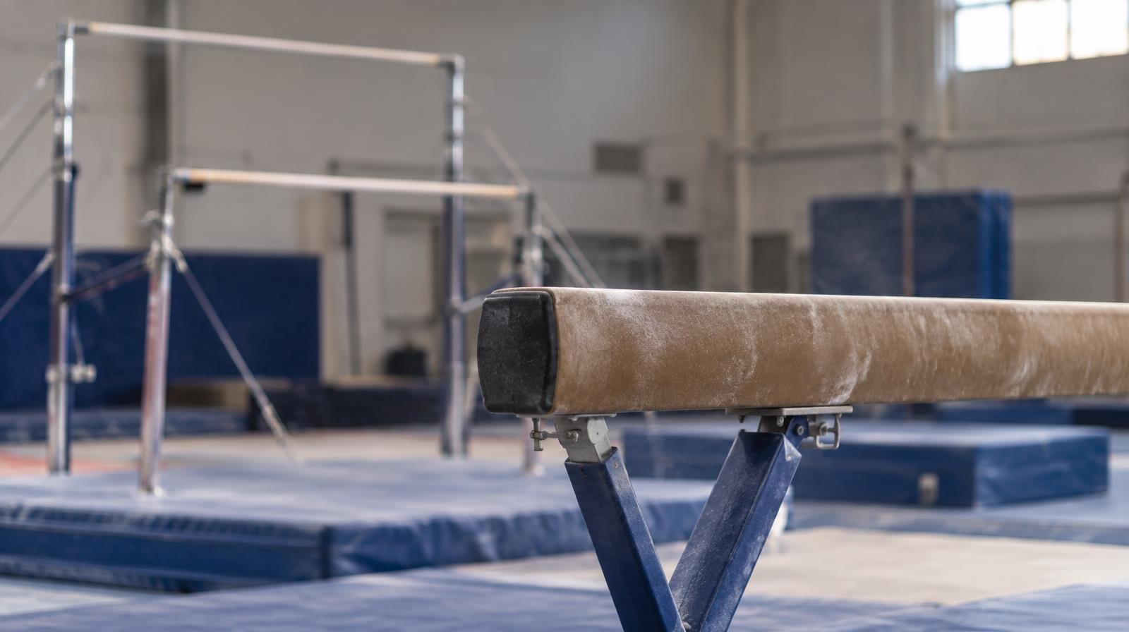 Empty gymnasium with a balance beam and uneven bars apparatus on the floor.