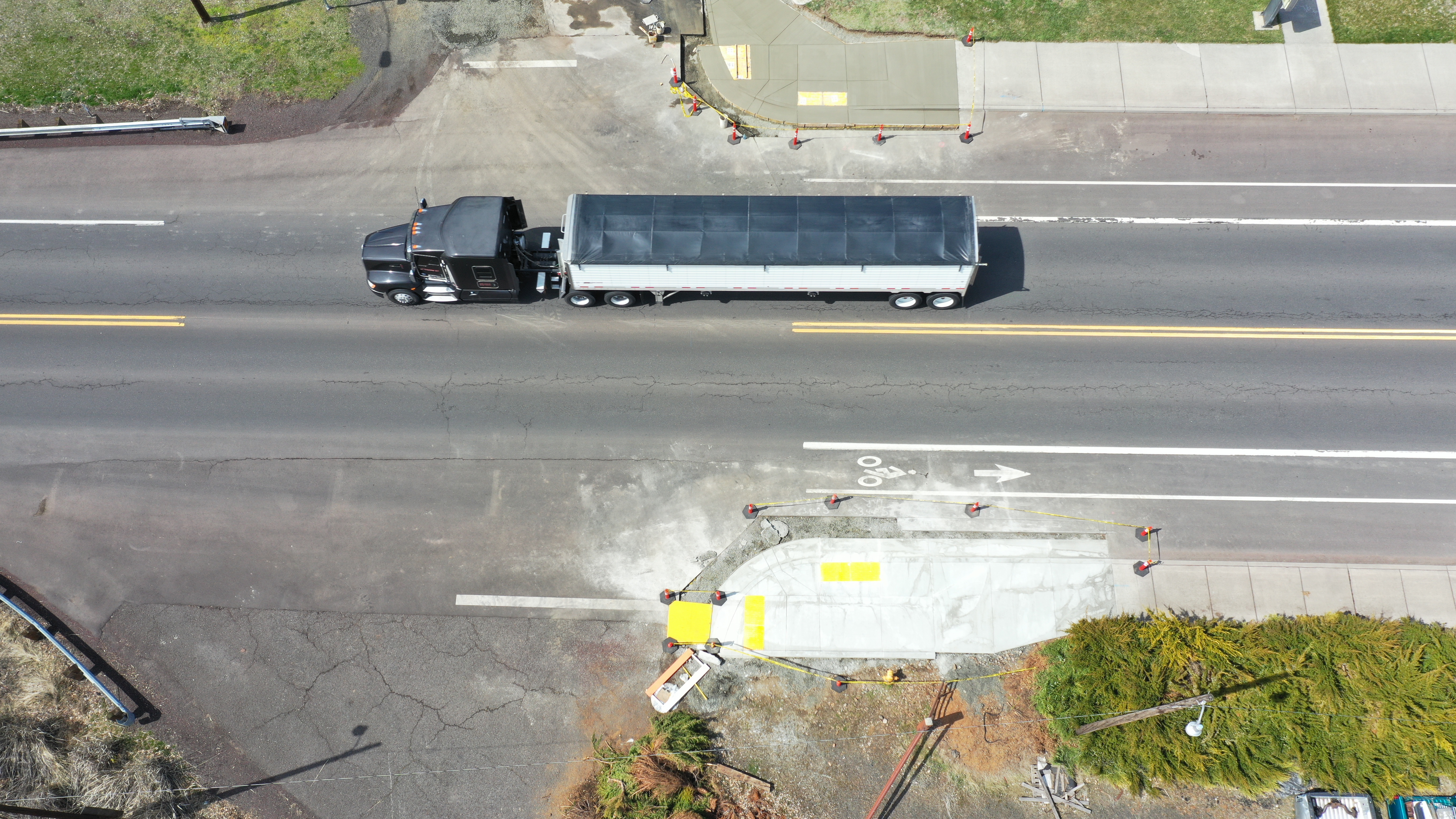 Aerial view of a new concrete curb ramp with yellow tactile paving at a road intersection.