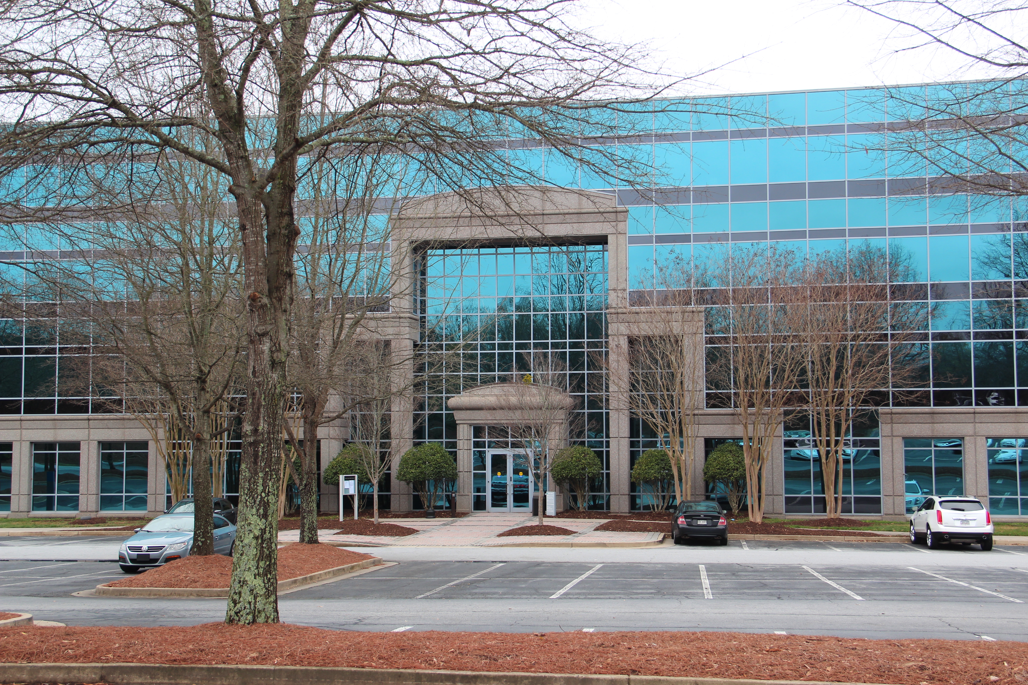 Multi-story government building with blue-green glass facade and bare trees in front.