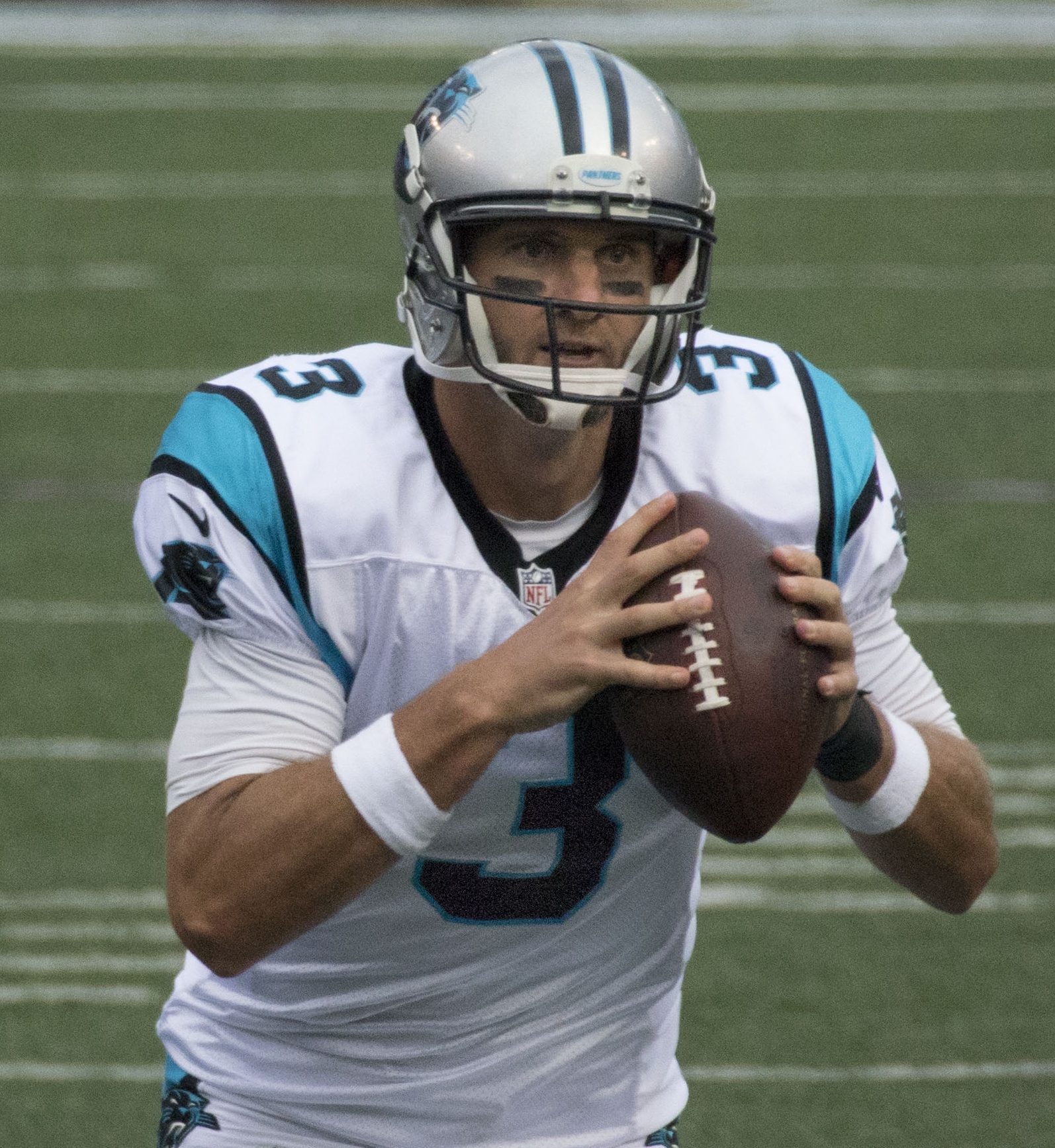 A football player in a white Carolina Panthers uniform holds a football ready to throw.