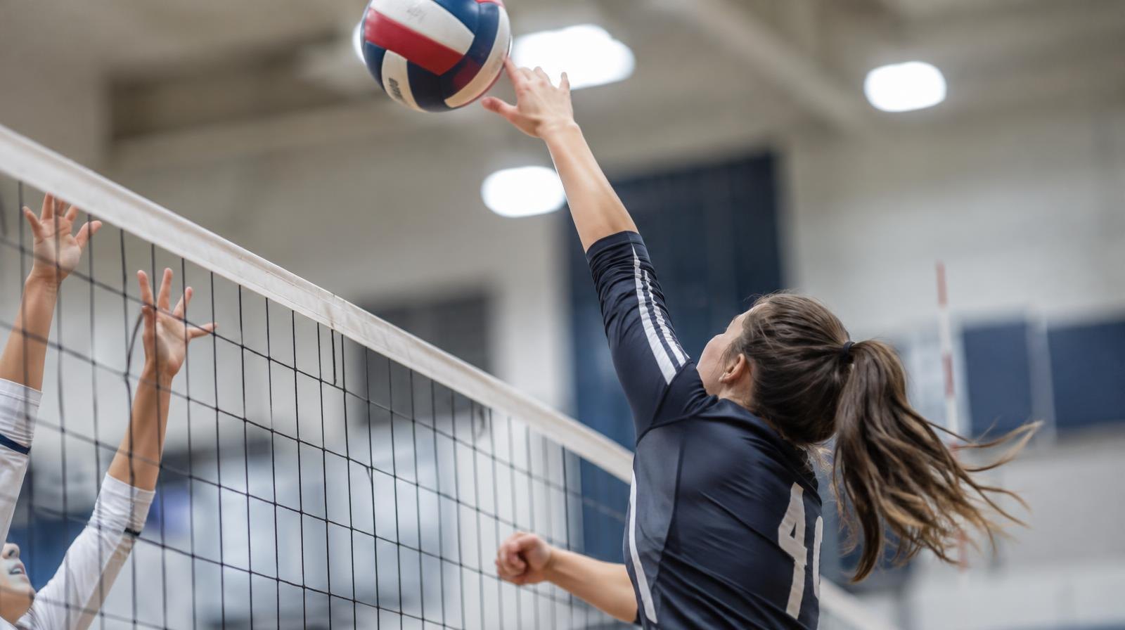 A volleyball player jumps at the net with arms extended to spike the ball.