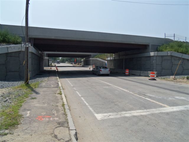 Concrete highway overpass with orange construction barrels blocking a lane below.