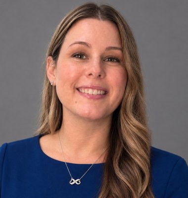 Woman with long brown hair smiling in a professional headshot against a gray background.