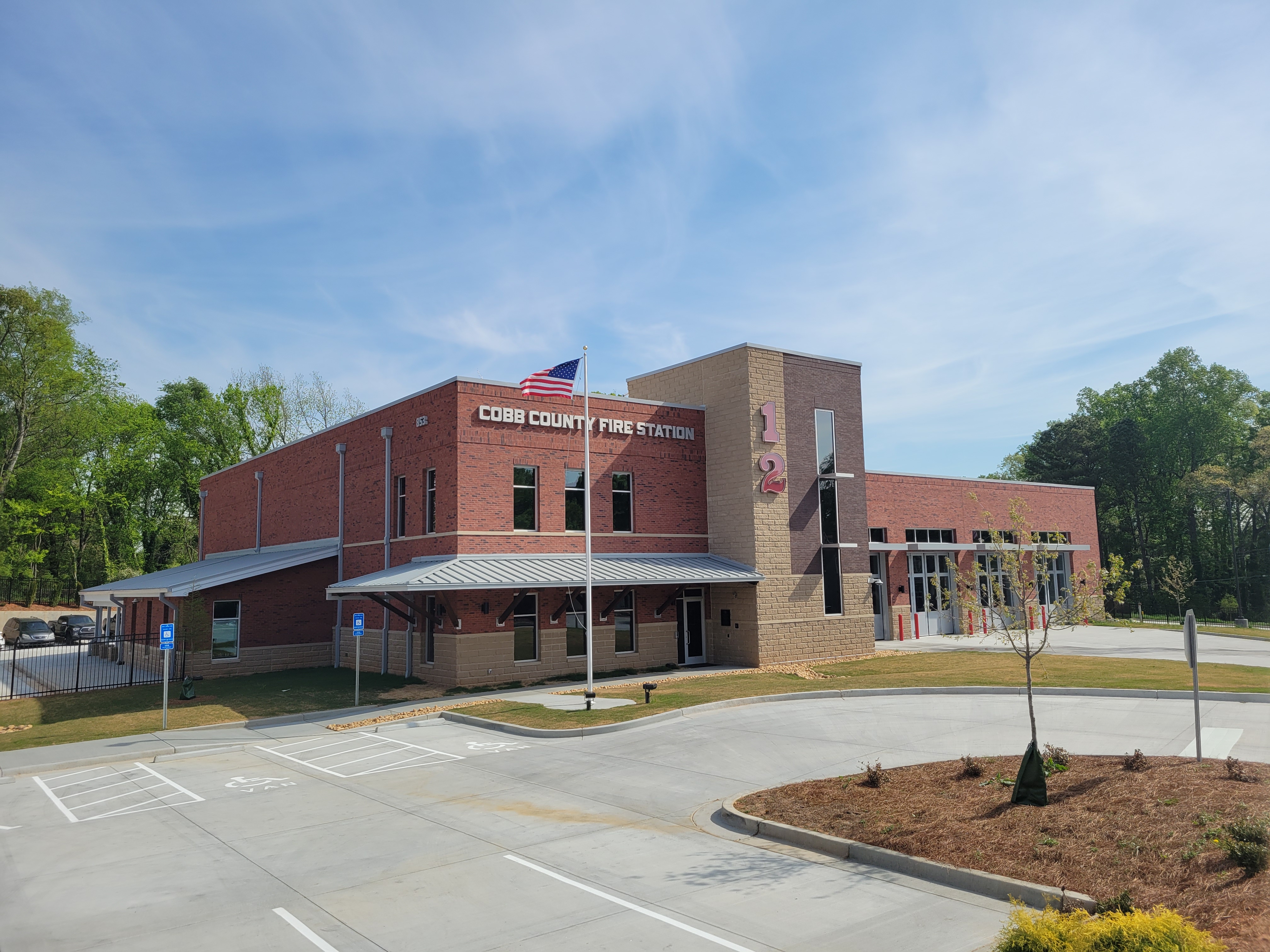 Modern brick fire station with large apparatus bay doors and a flagpole outside.