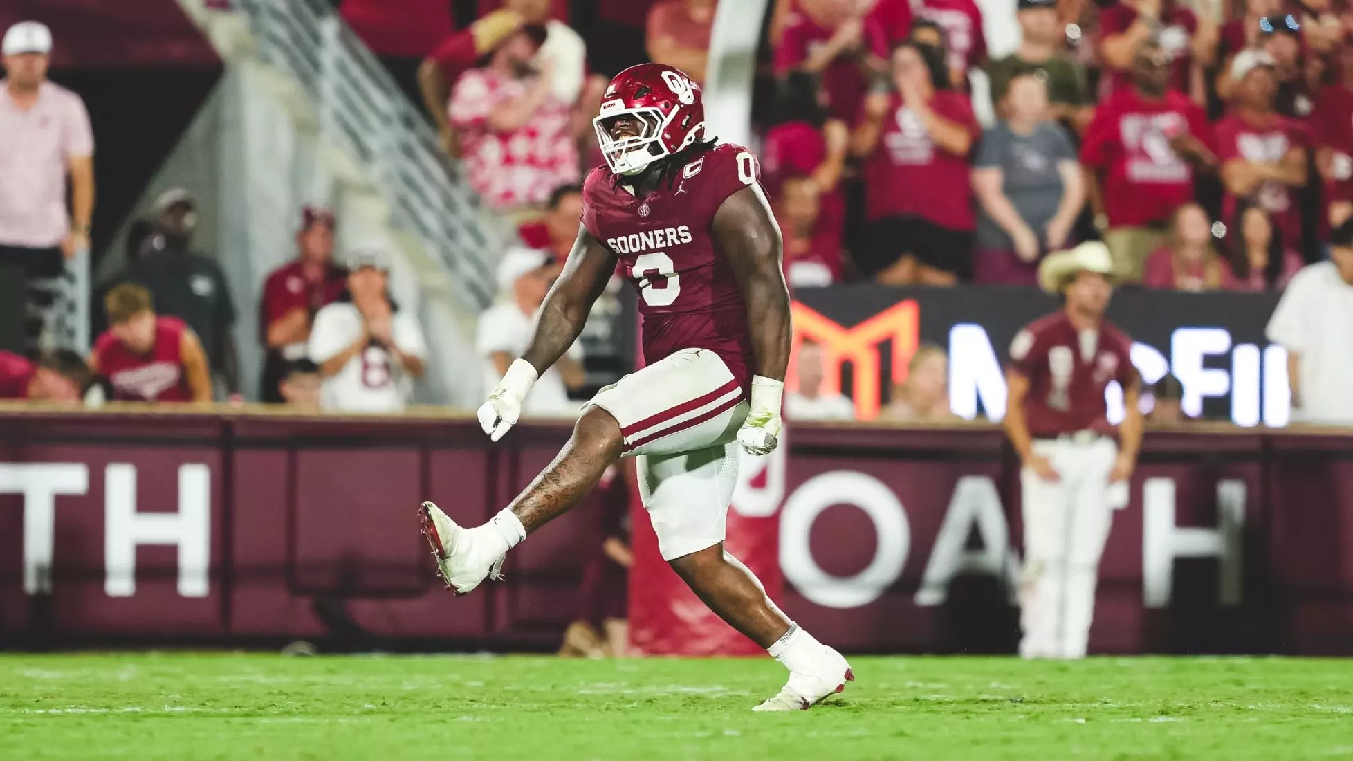 Football player in crimson Sooners uniform celebrating on the field at night.