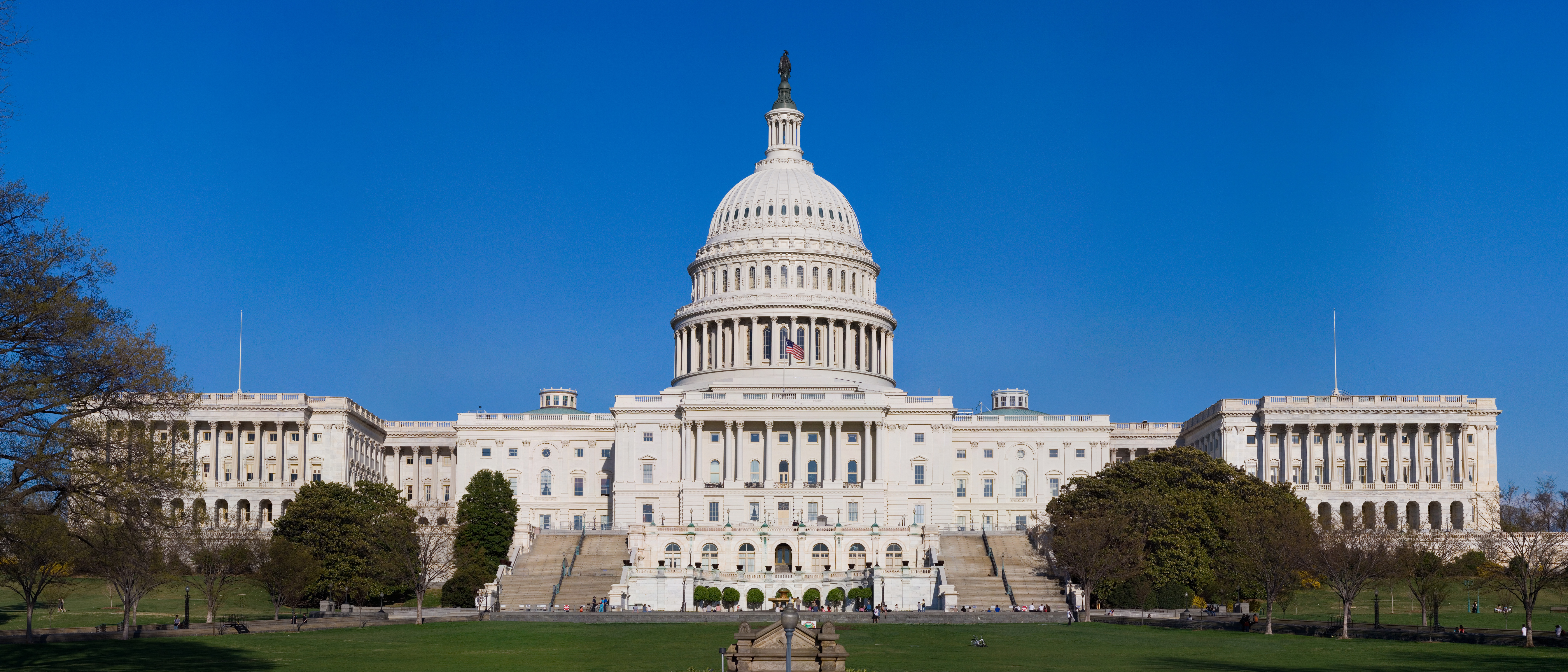 The west front of the U.S. Capitol building under a clear blue sky with green lawns.