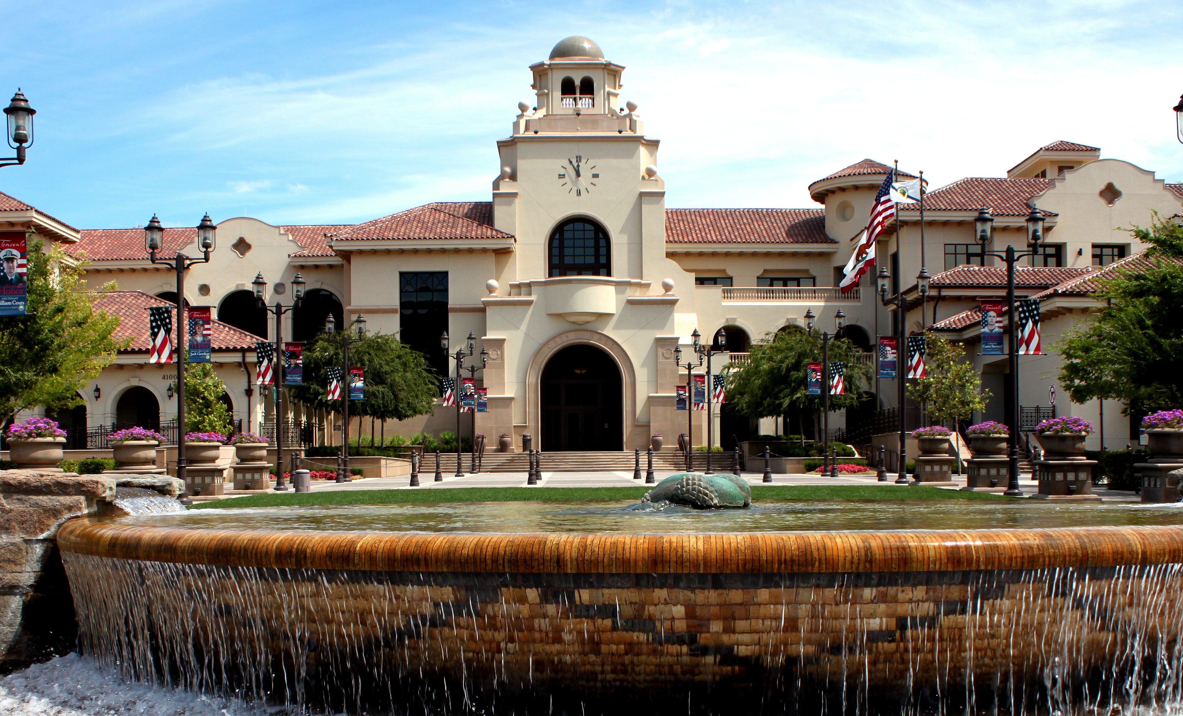 Temecula City Hall exterior with clock tower, fountain, and American flags.