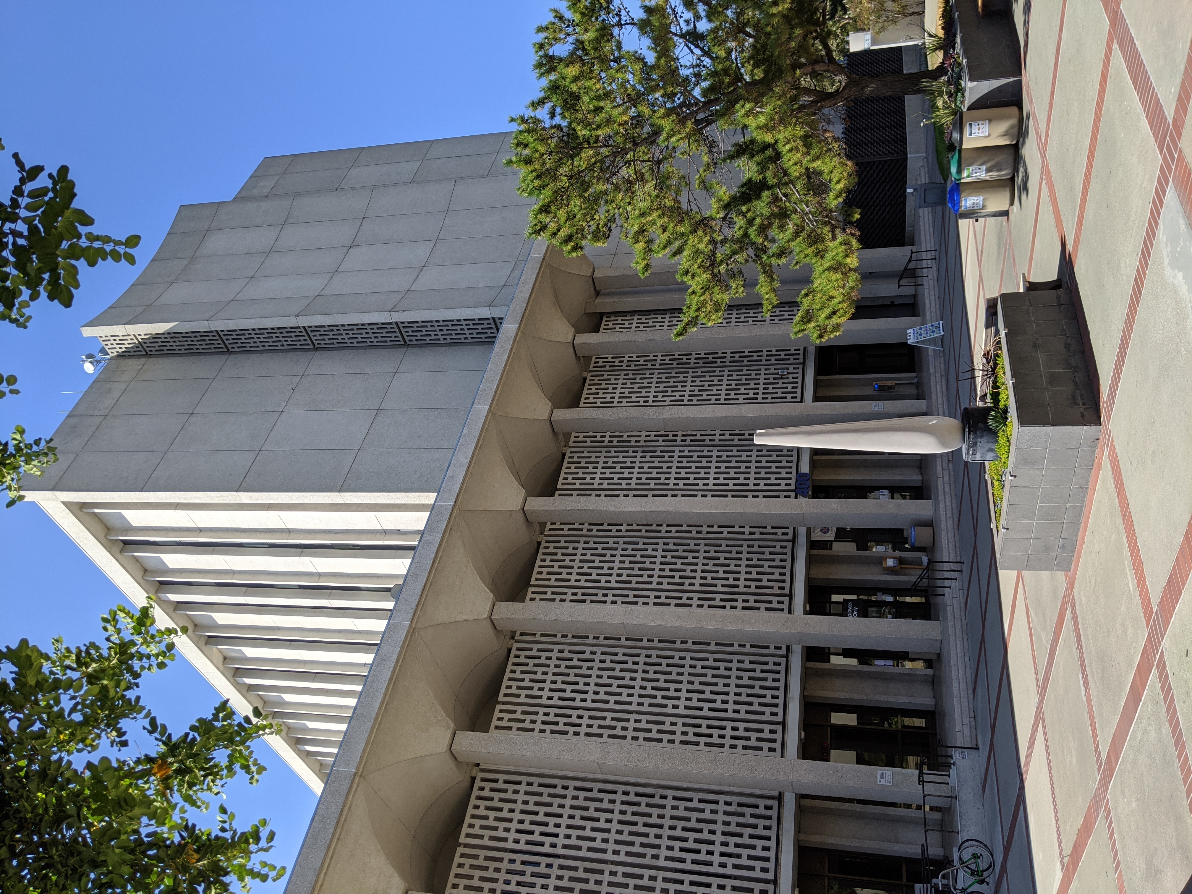 Brutalist concrete government building with tall tower and colonnaded facade in a plaza.