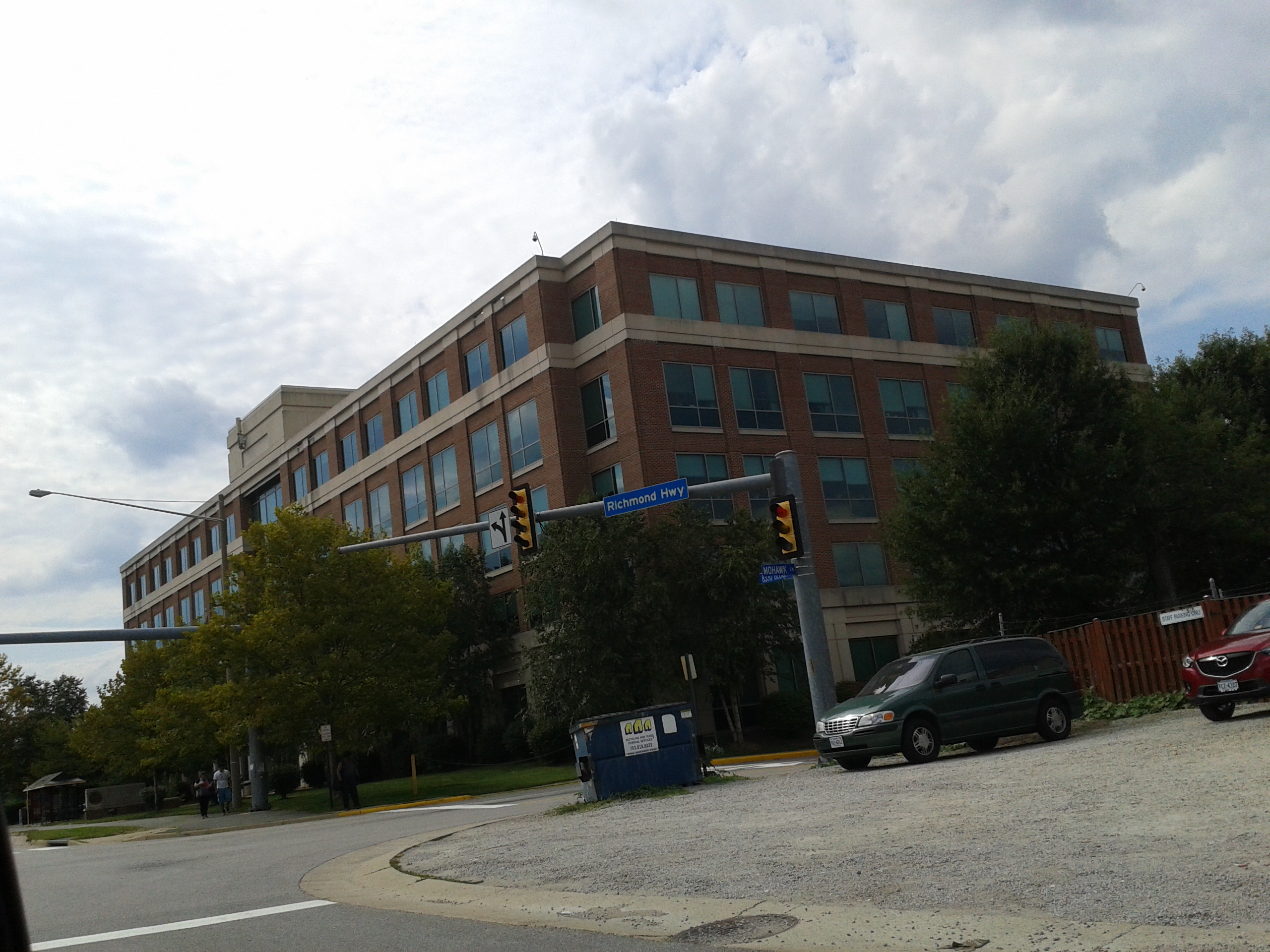 Multi-story brick government office building at a street corner with traffic signals and trees.