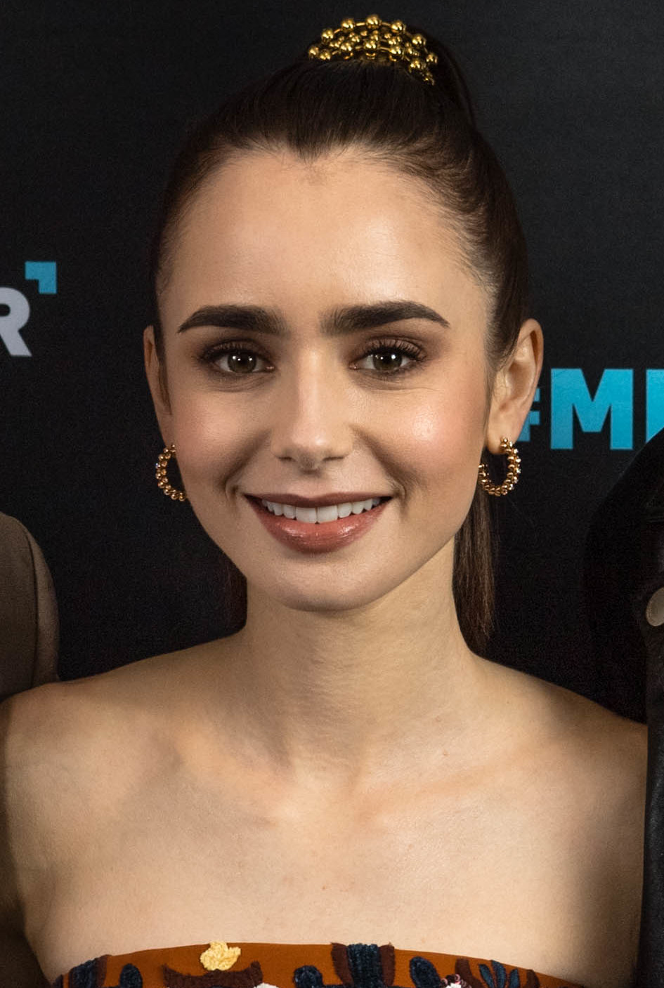 Lily Collins with dark hair in a ponytail smiling at a film festival event.