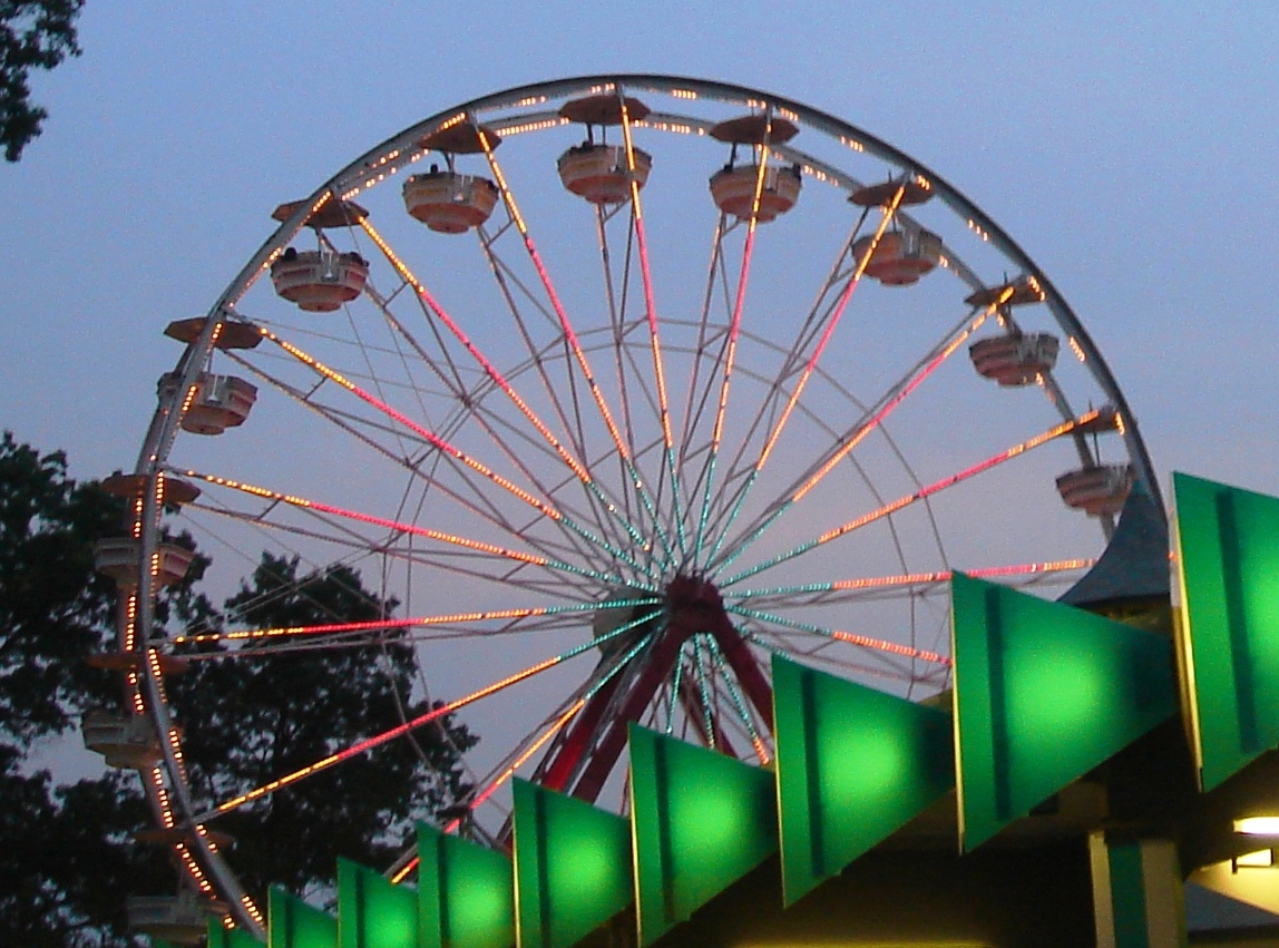 Illuminated Ferris wheel with gondola cars glowing at dusk at an amusement park.