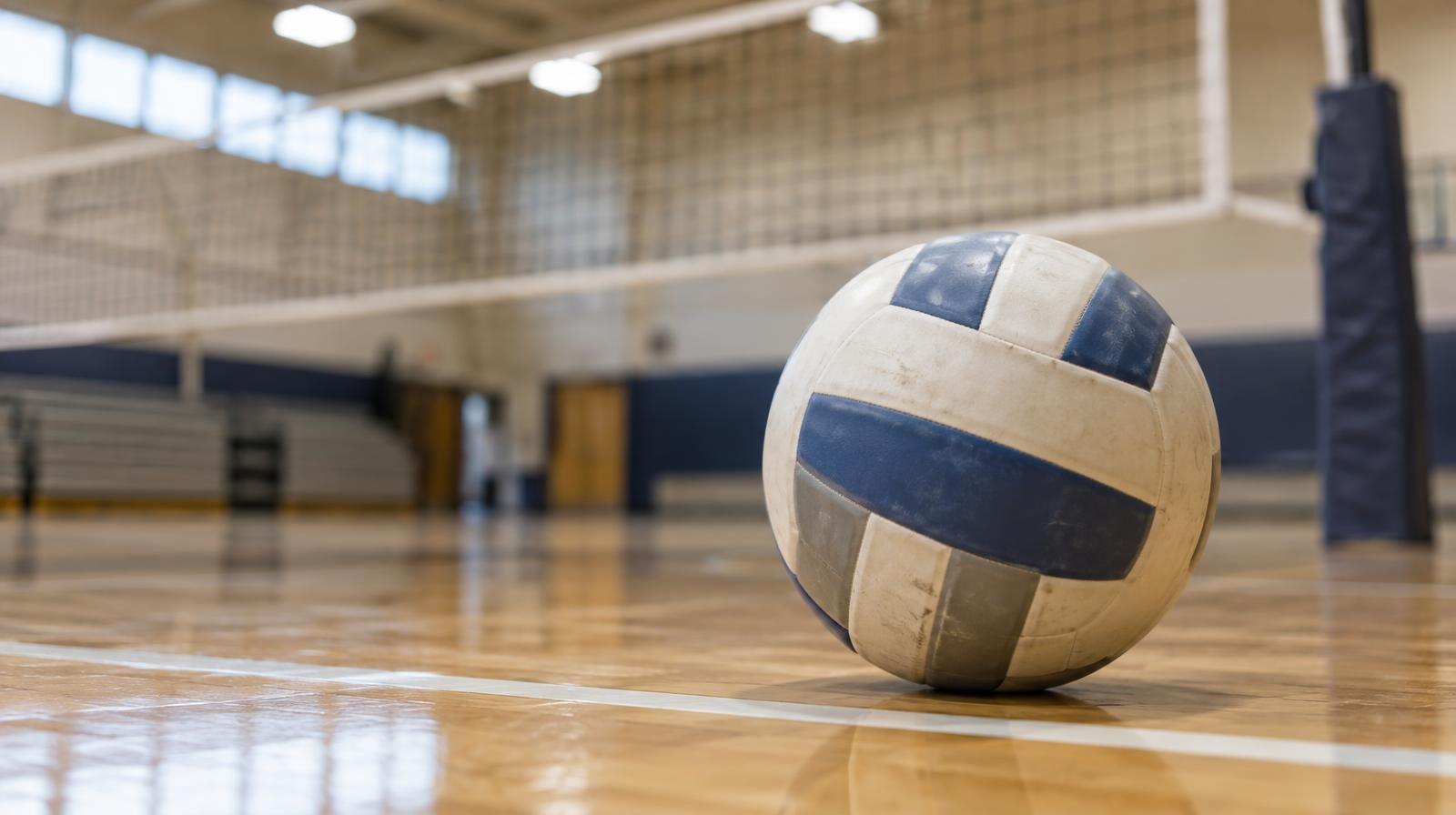 A volleyball resting on a hardwood gymnasium floor near a net.