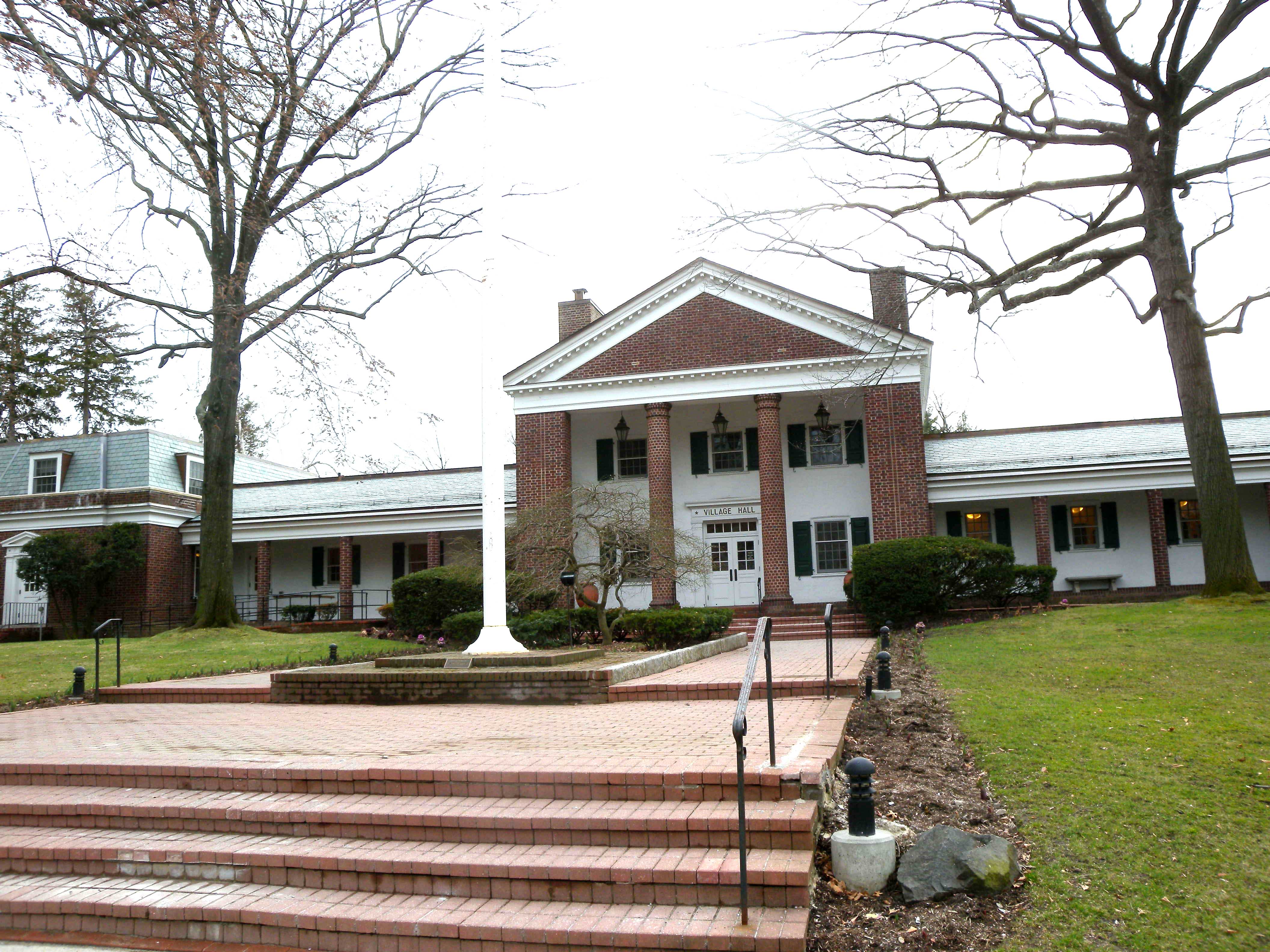Brick colonial building with white columns and pediment, flanked by wings with white siding, on a cloudy day.