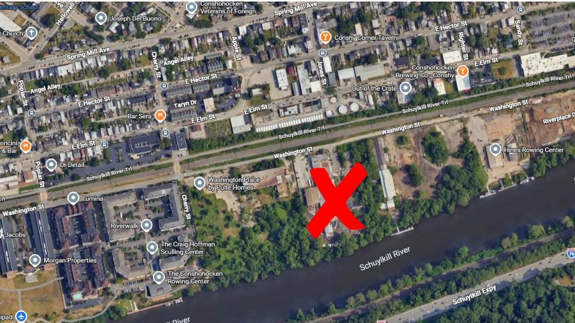 Satellite map with a red X marking an industrial parcel along a river near labeled streets.