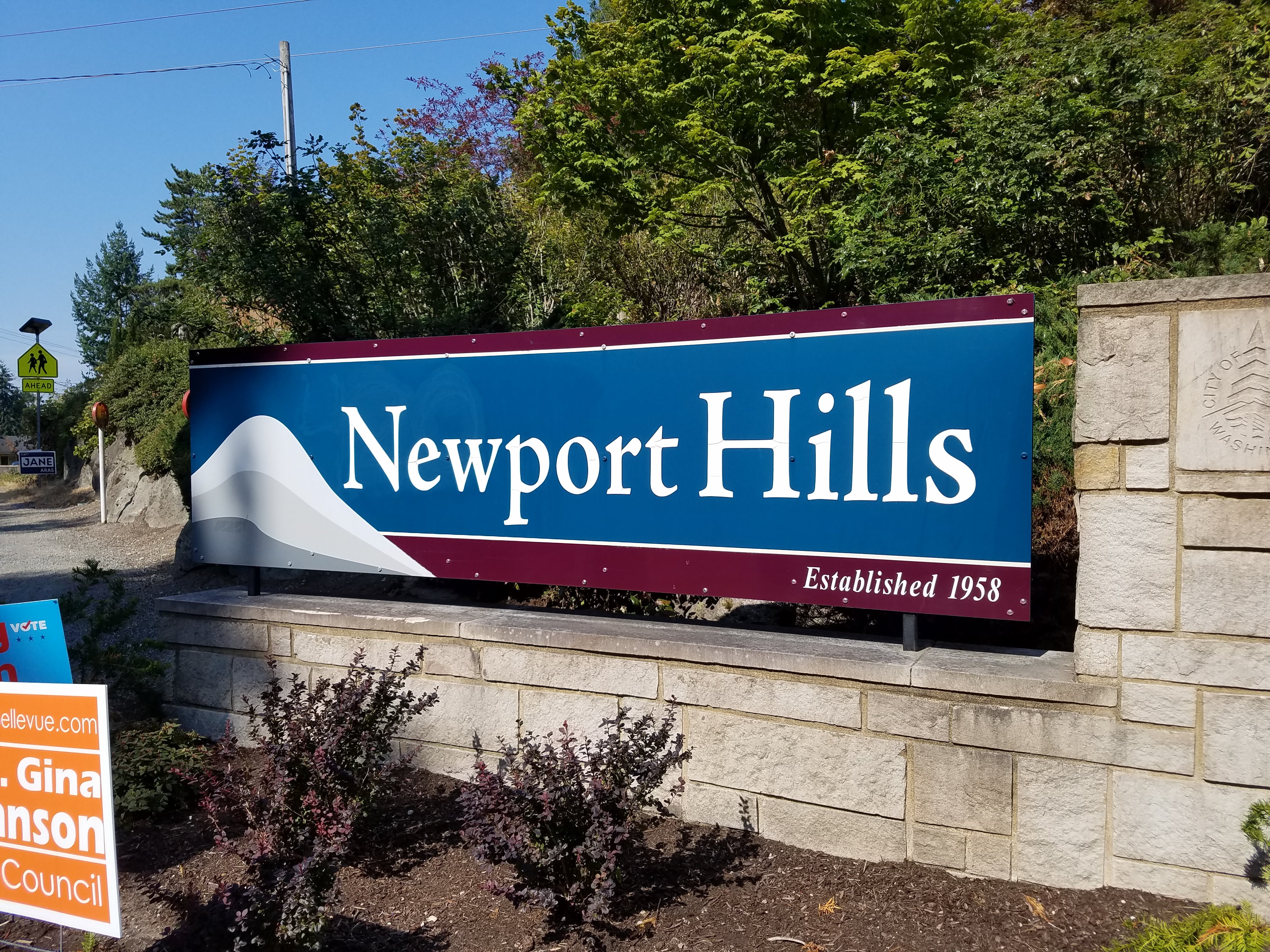 Stone-mounted neighborhood sign reading Newport Hills, surrounded by trees and shrubs.