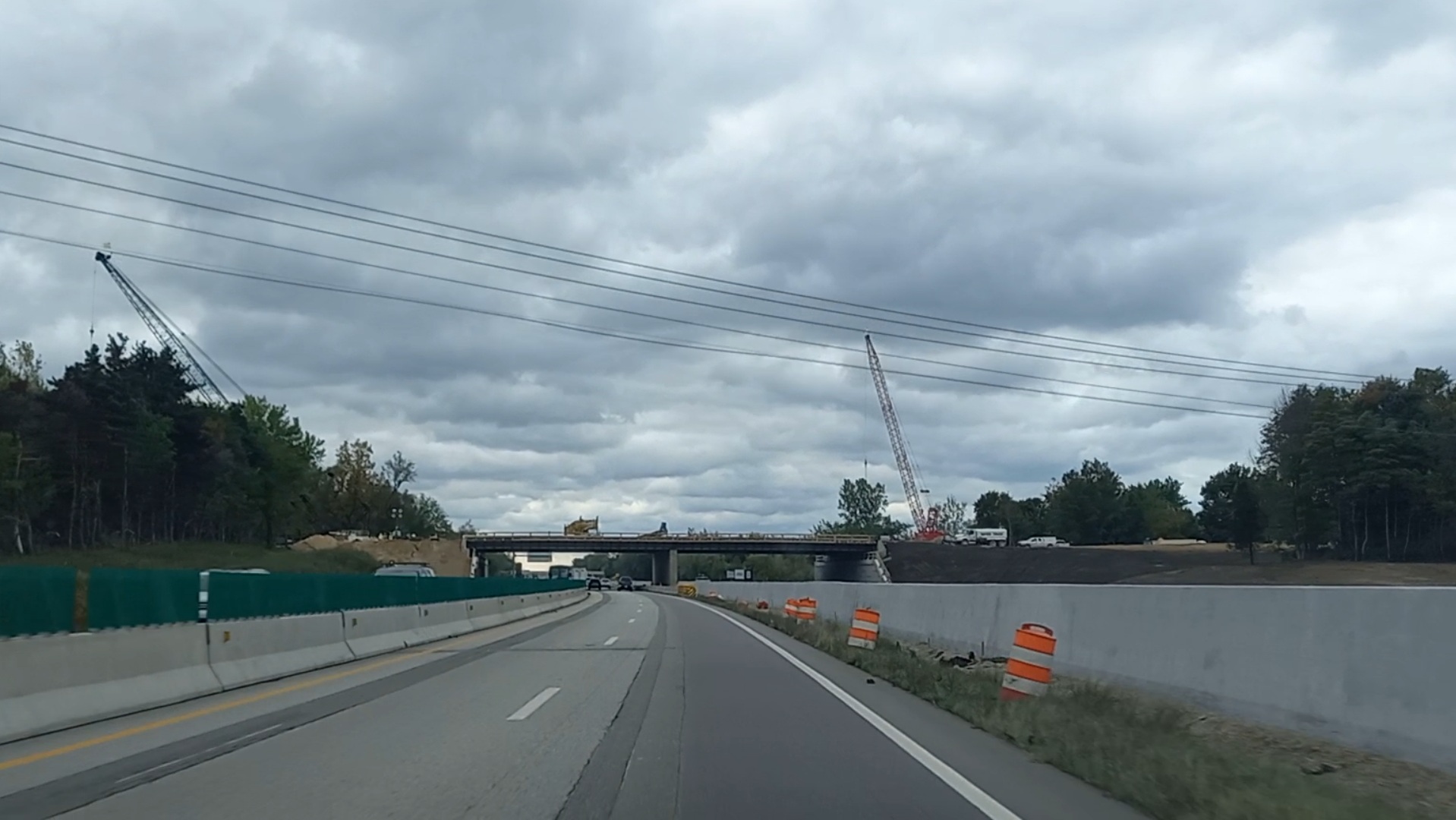 Interstate highway under construction with cranes, green barrier walls, and orange barrels.