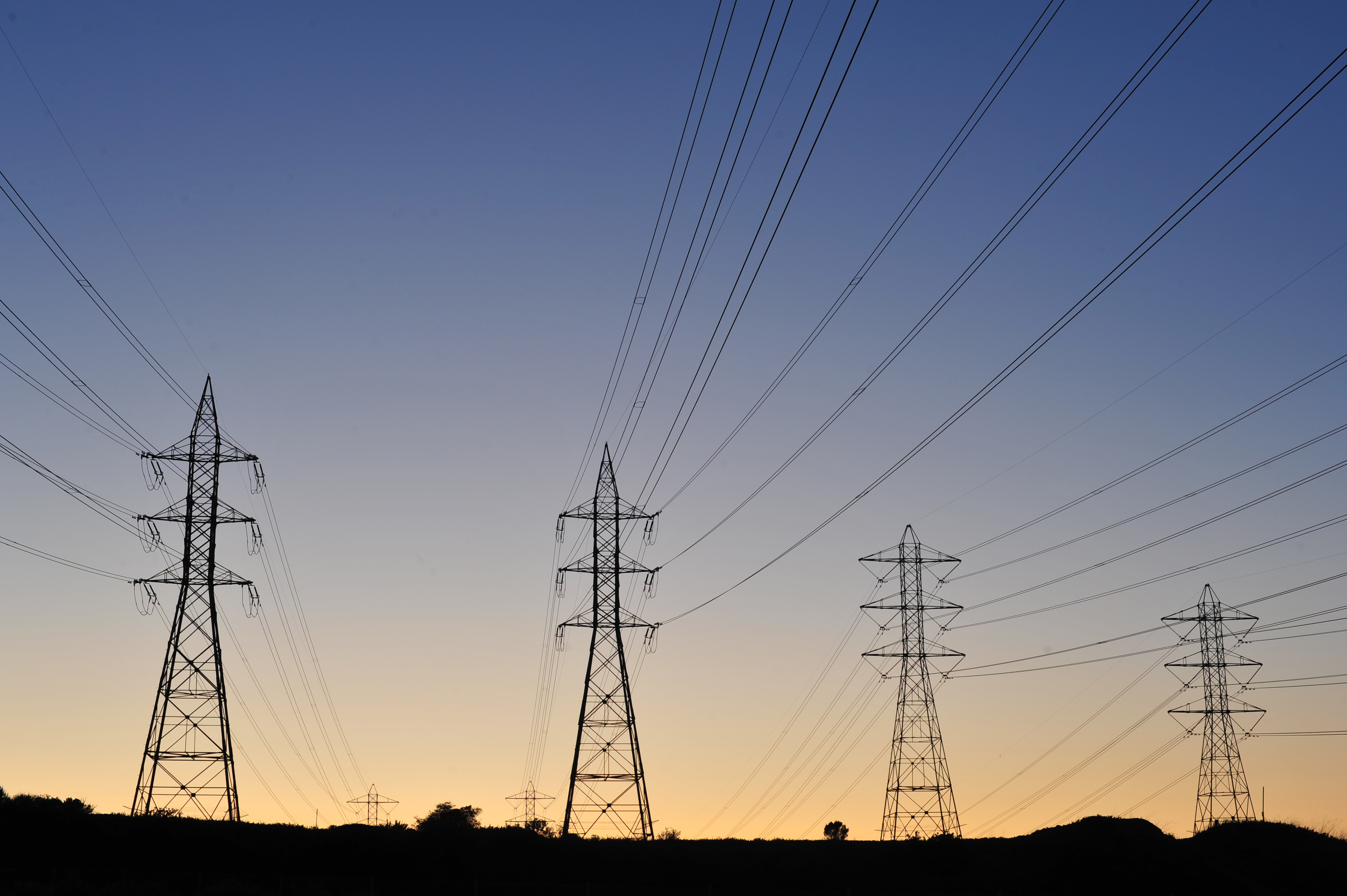 High-voltage electric transmission towers silhouetted against a twilight sky.