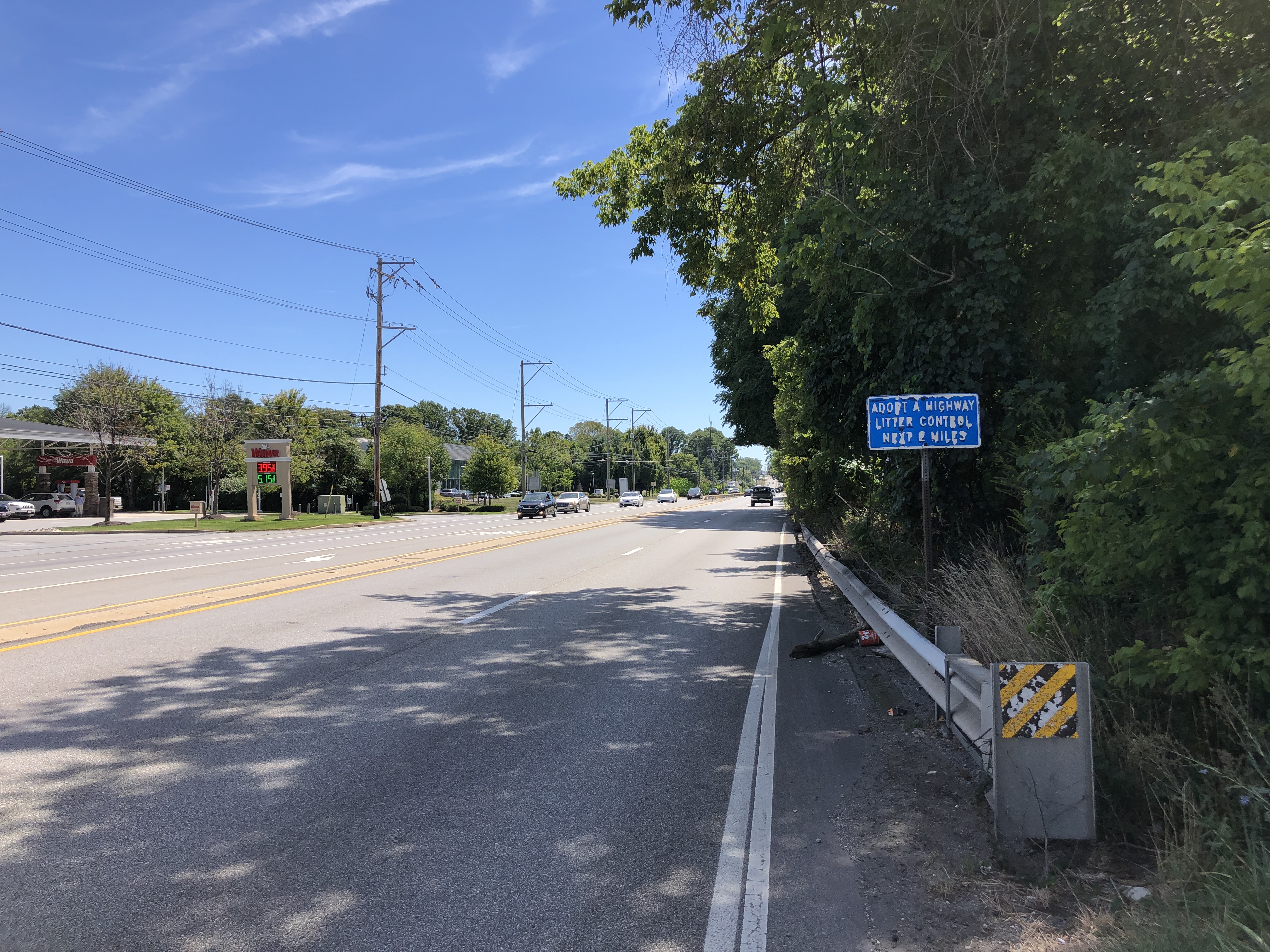 Multi-lane highway with a blue sign, guardrail, and sparse traffic under blue sky.