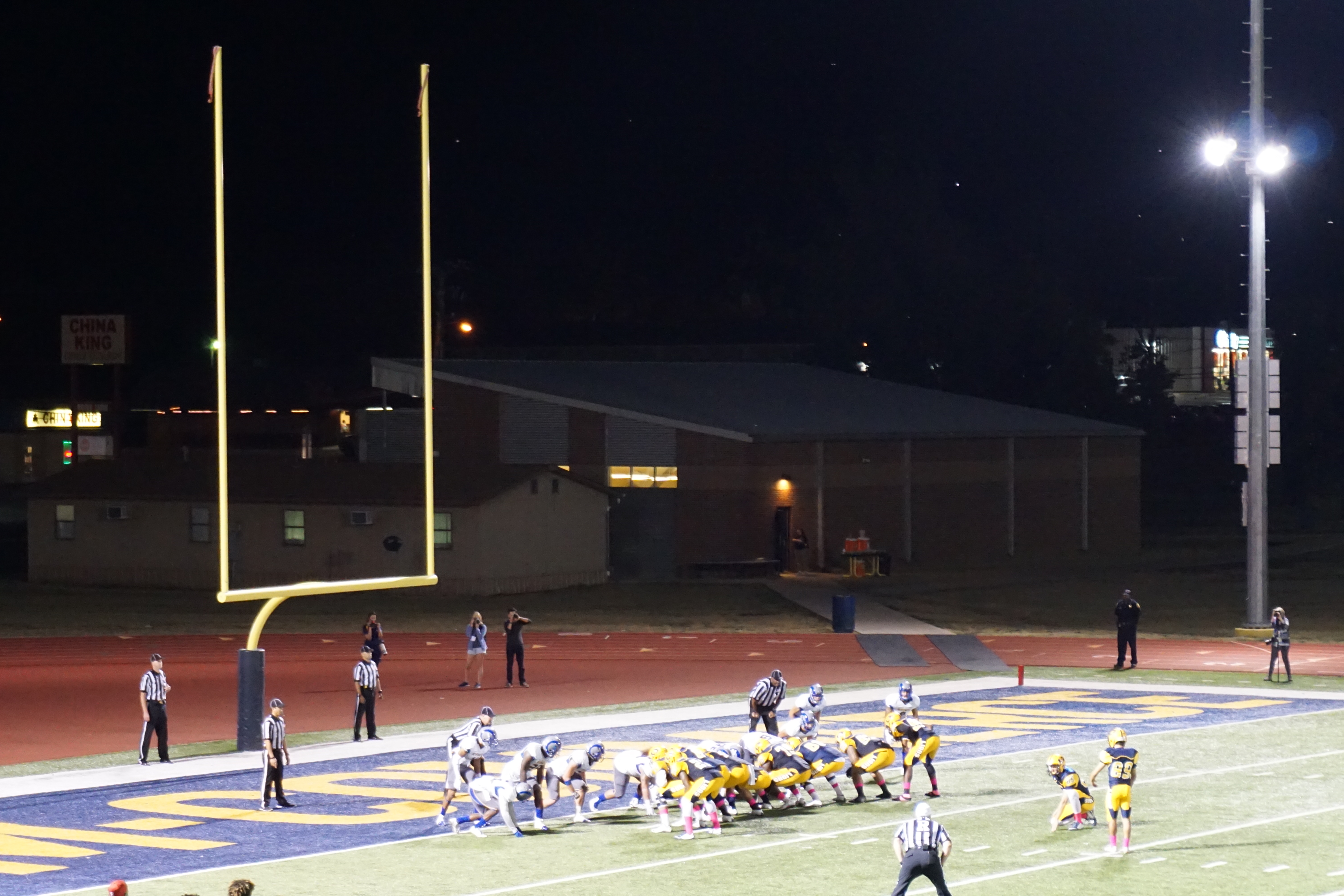 Football players lined up near an end zone under stadium lights at night.