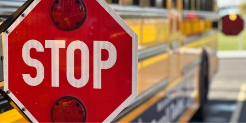 Red stop sign extended from the side of a yellow school bus.