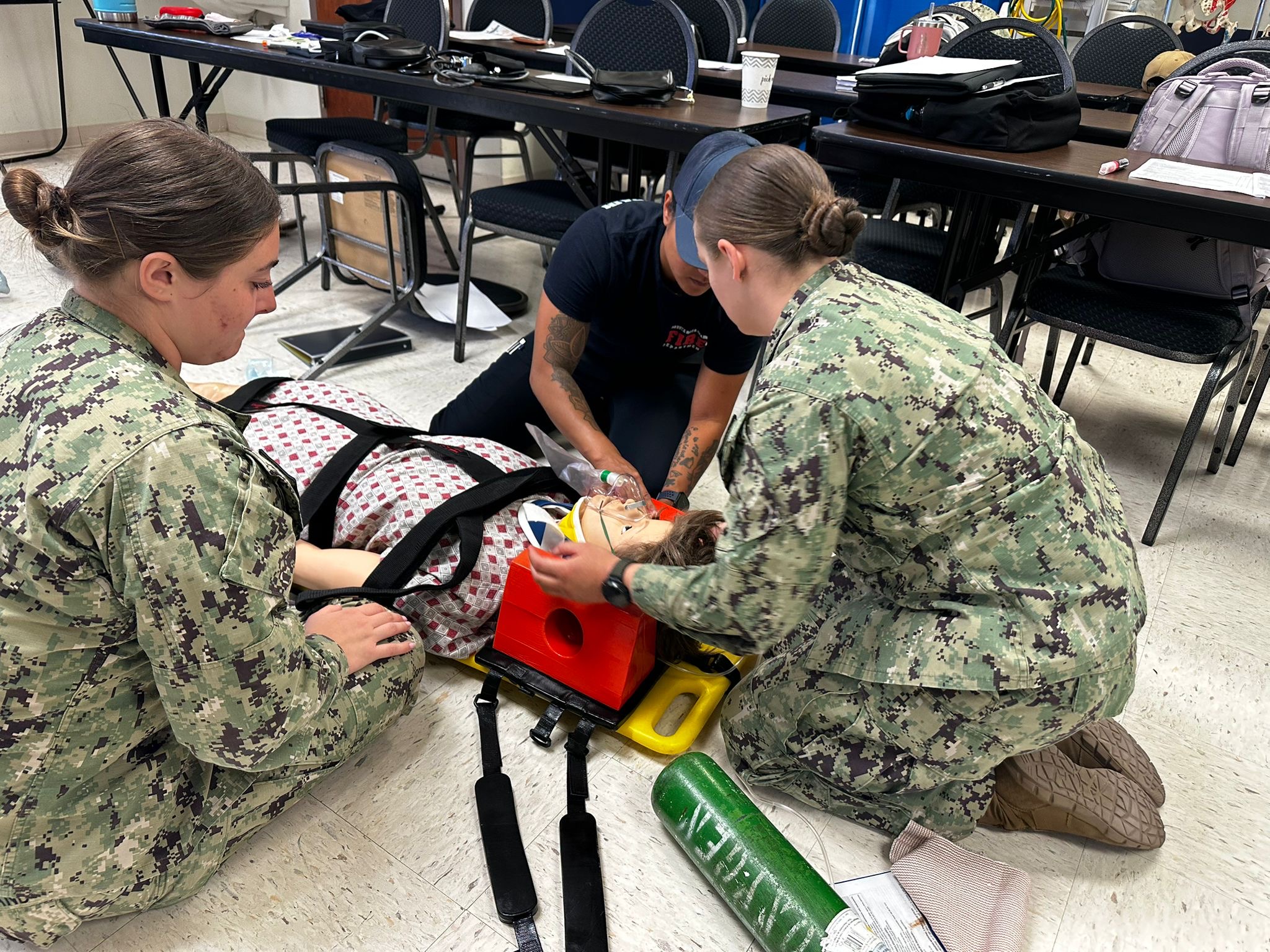 Trainees in a classroom practice airway management on a medical training mannequin on a stretcher.