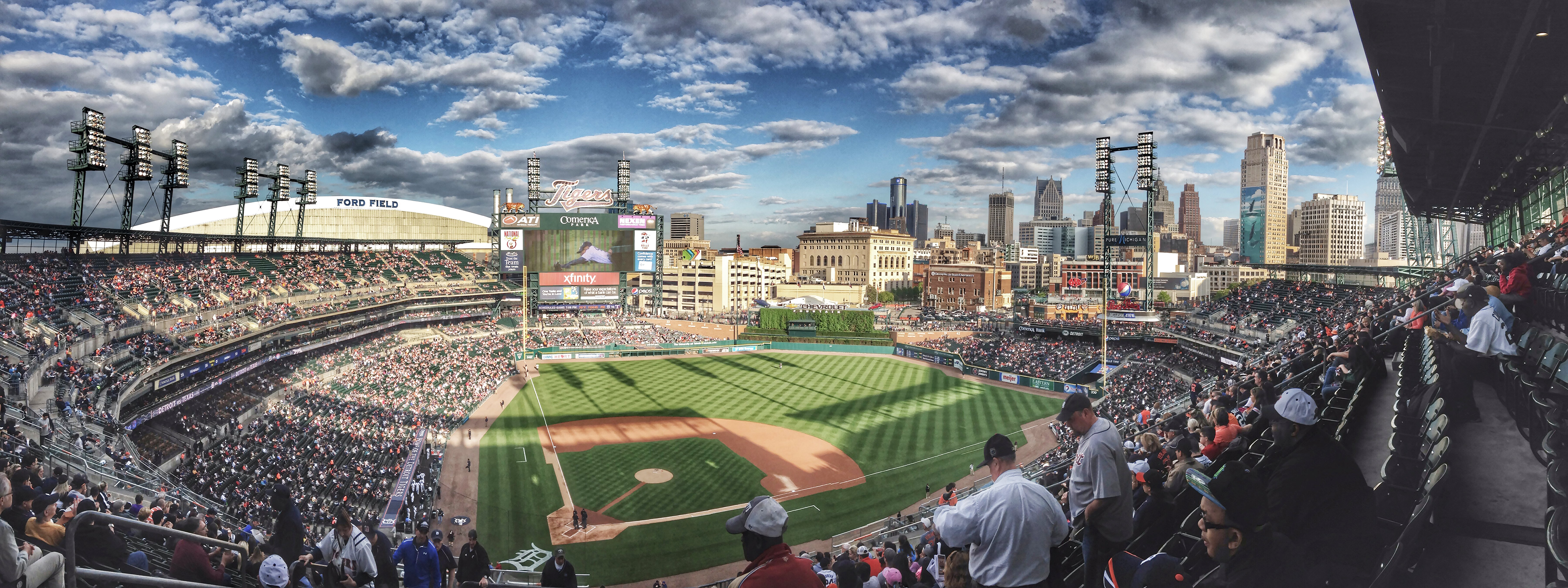 Panoramic view of a baseball stadium filled with fans, city skyline visible beyond the outfield.