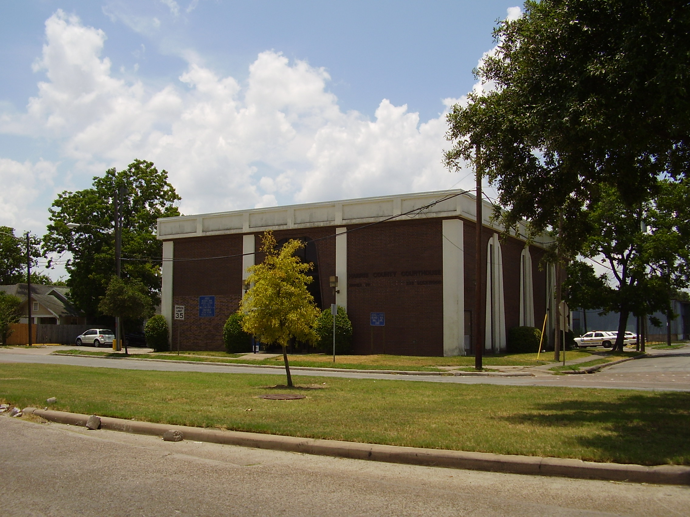 Single-story brick Harris County government building surrounded by trees and lawn.