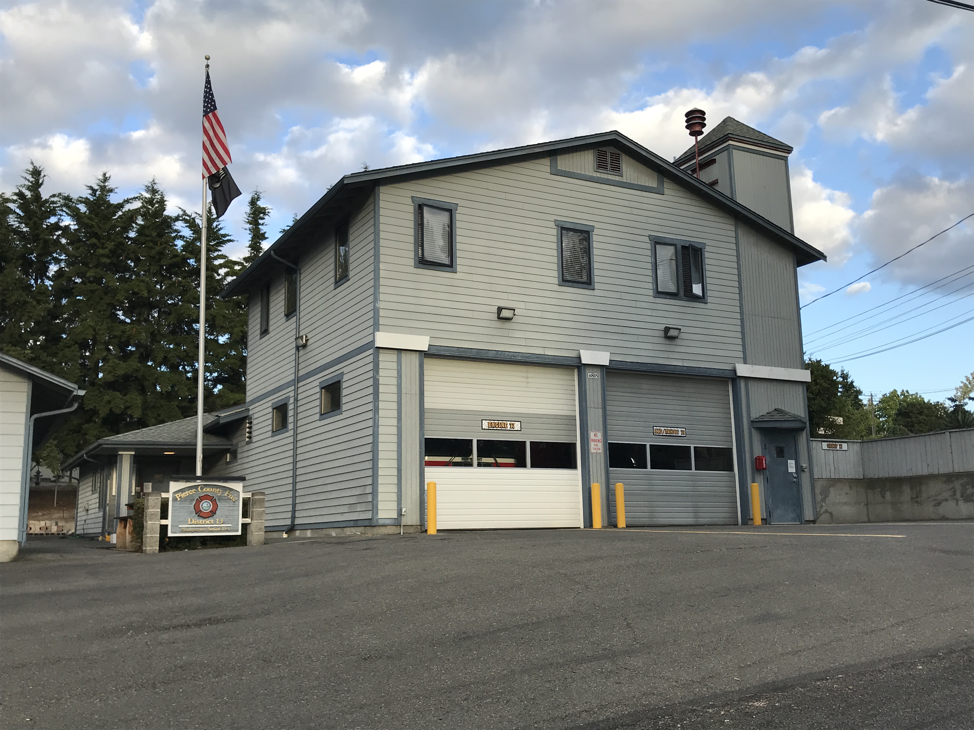 Two-story gray fire station with two roll-up garage doors and an American flag on a pole.