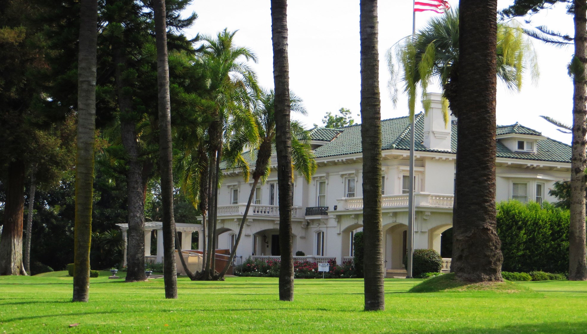 A large white Italian Renaissance-style mansion with palm trees and a manicured lawn.