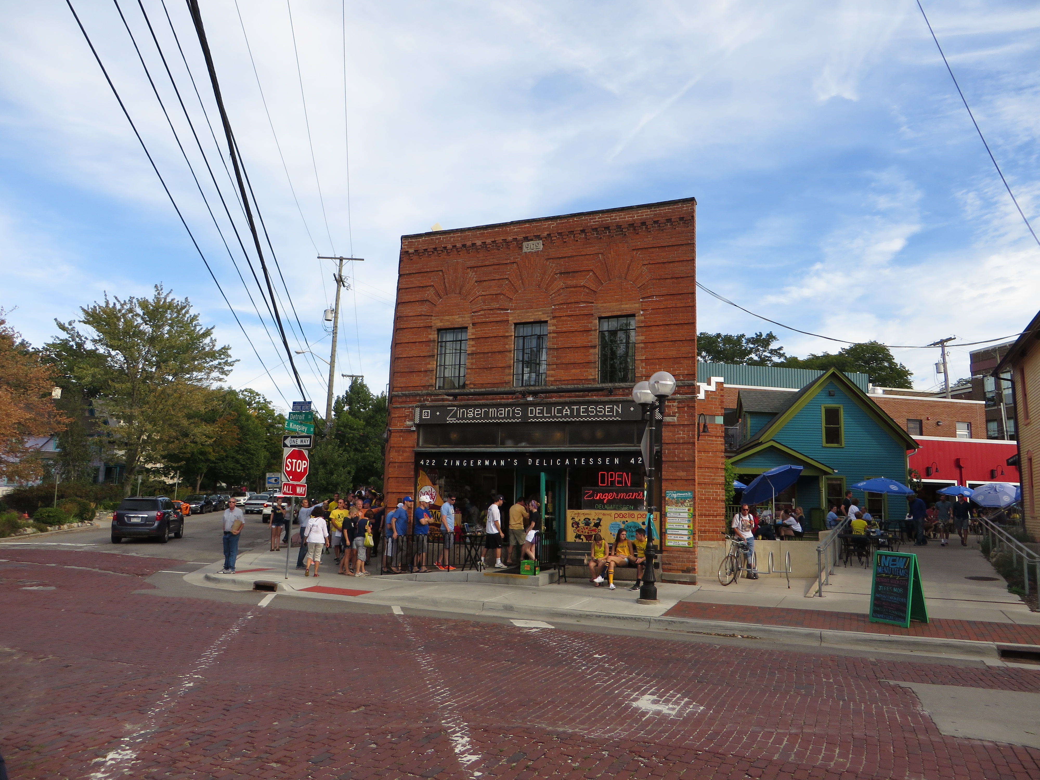 Red brick corner building with a crowd of customers lined up outside on a sunny day.